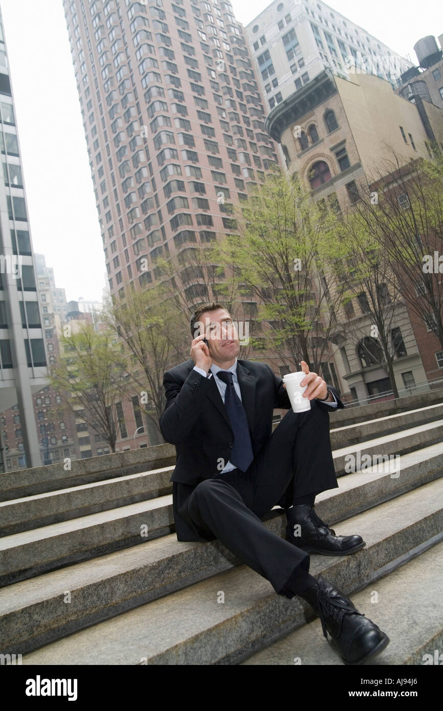 Geschäftsmann, sitzen auf Stufen mit Handy und halten Tasse Kaffee Stockfoto