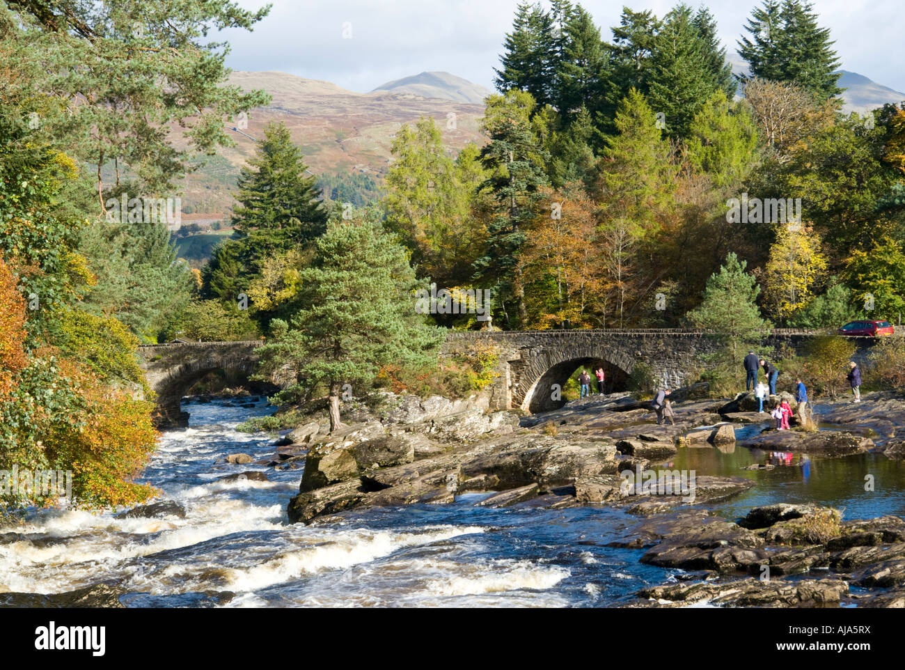 Mehrere kleine Wasserfälle am Fluss Dochart bei Killin mit Dochart Flussbrücke an einem sonnigen Herbsttag Stockfoto