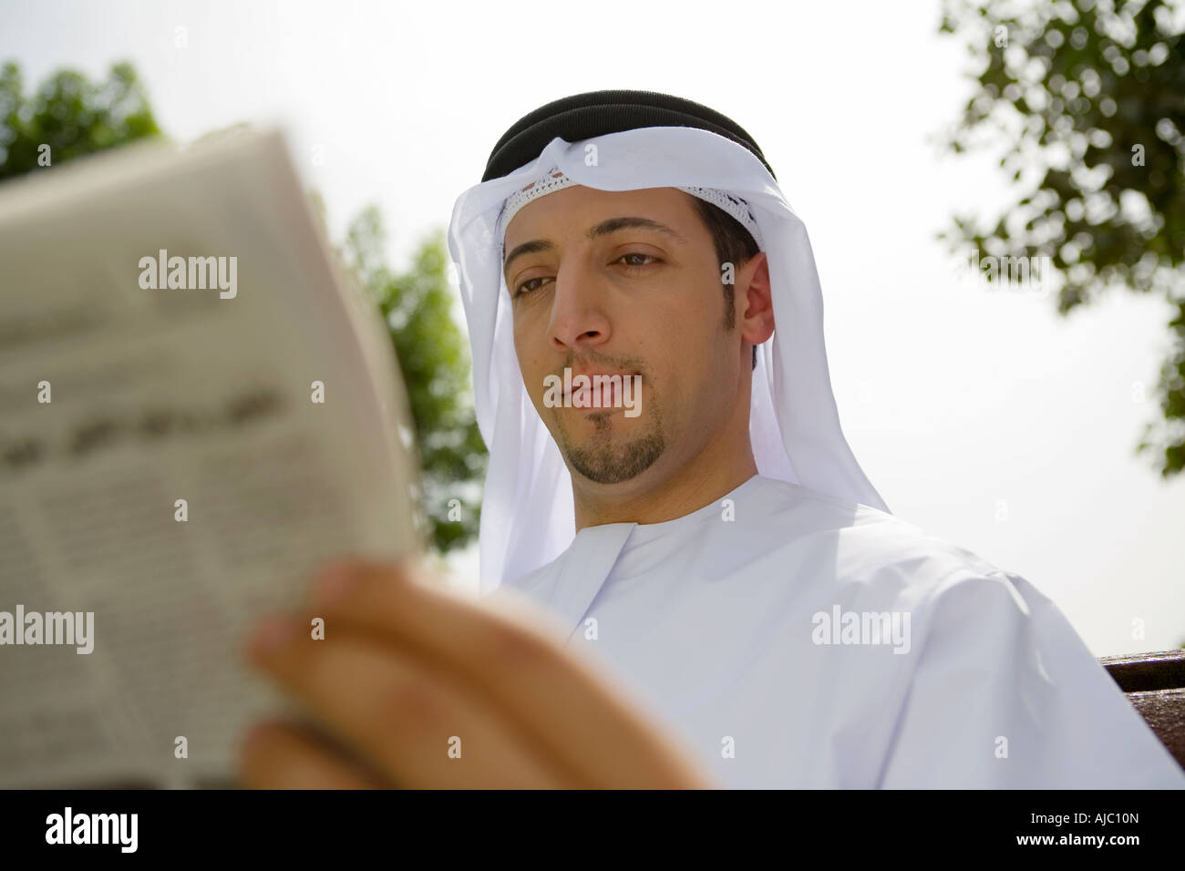 Arabische Mann lesen Zeitung auf Parkbank Stockfoto