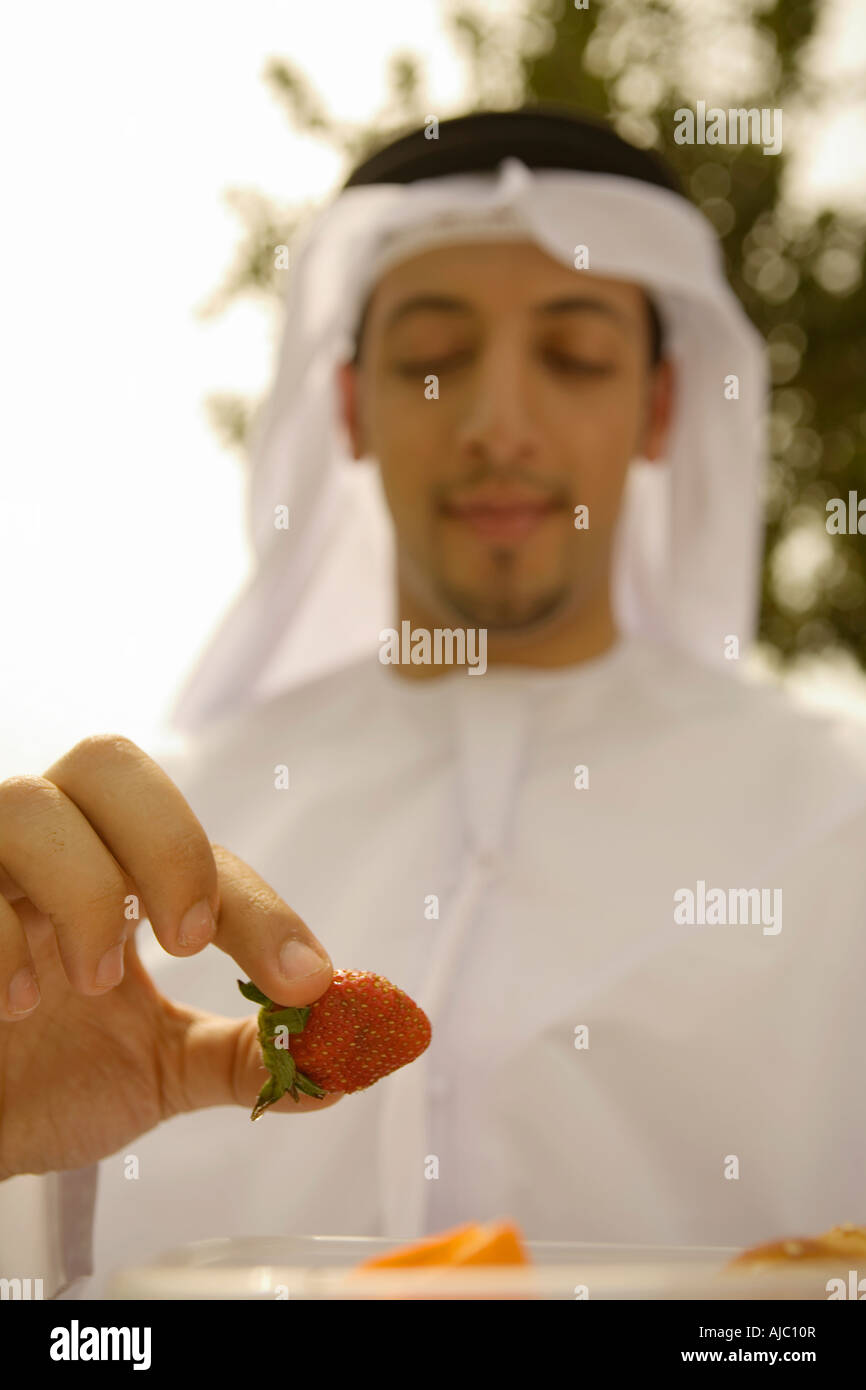 Lächelnder Arabische Mann Essen Erdbeere auf Parkbank, Low Angle View Stockfoto