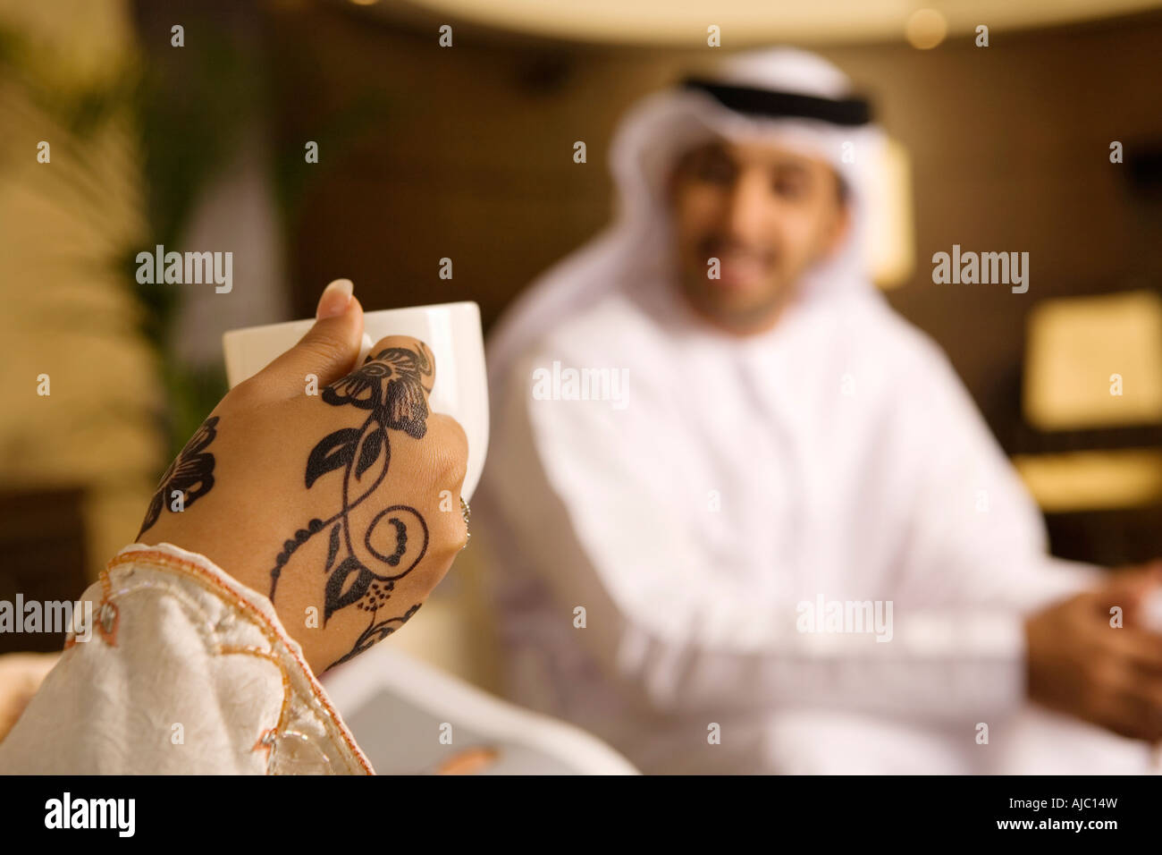 Arabische Frau mit Henna auf Hände halten Kaffeetasse, lächelnd Arabische Mann im Wohnzimmer Stockfoto