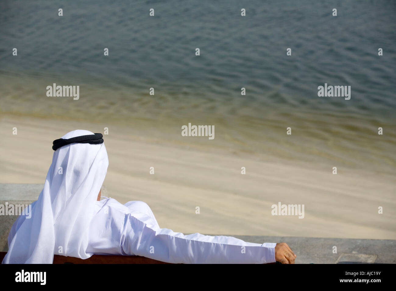 Arabische Mann sitzt auf der Parkbank, Blick auf Wasser Stockfoto