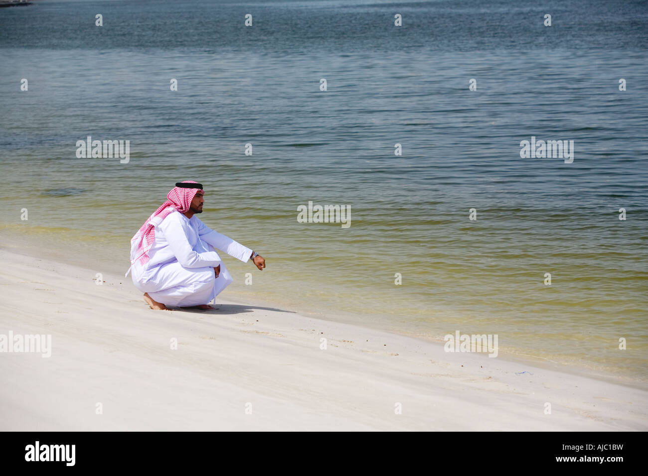 Arabische Mann hocken in den Sand Skipping Stones Stockfoto