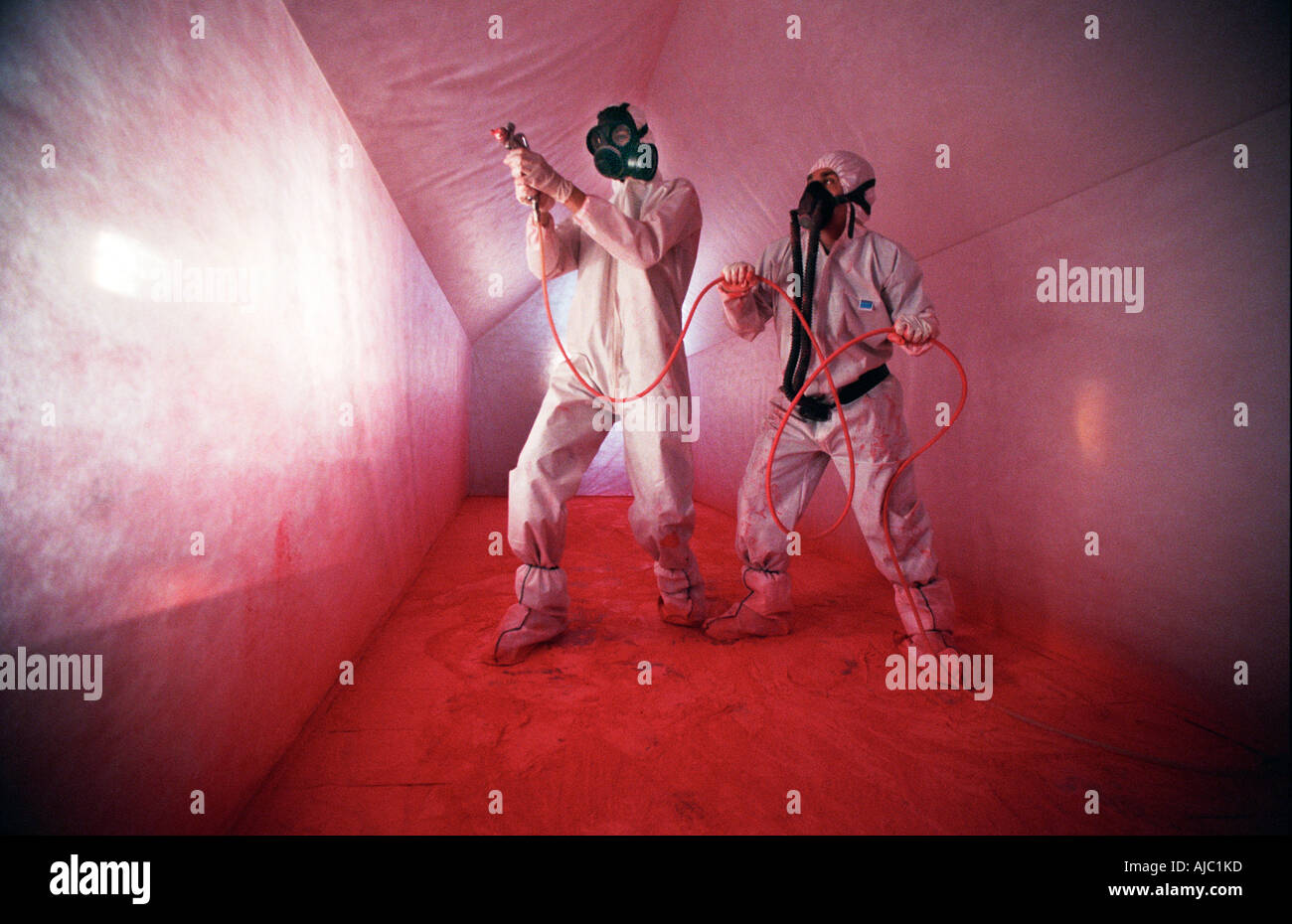 Zwei Performance-Künstler in weißen Kessel Anzügen und Masken sprühen roten Farbe in einem weißen Tunnel. Stockfoto