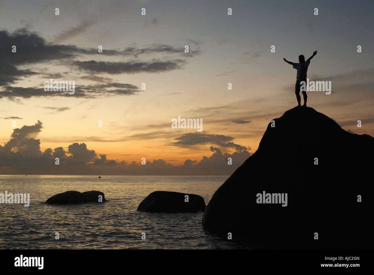 Silhouette einer Frau, die auf einem Felsen steht bei Sonnenuntergang Stockfoto
