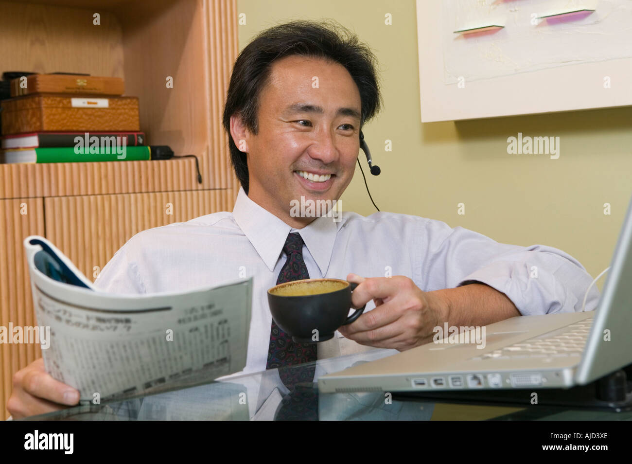 Geschäftsmann am Kopfhörer sprechen, mittels Laptop und lesen Zeitung Stockfoto