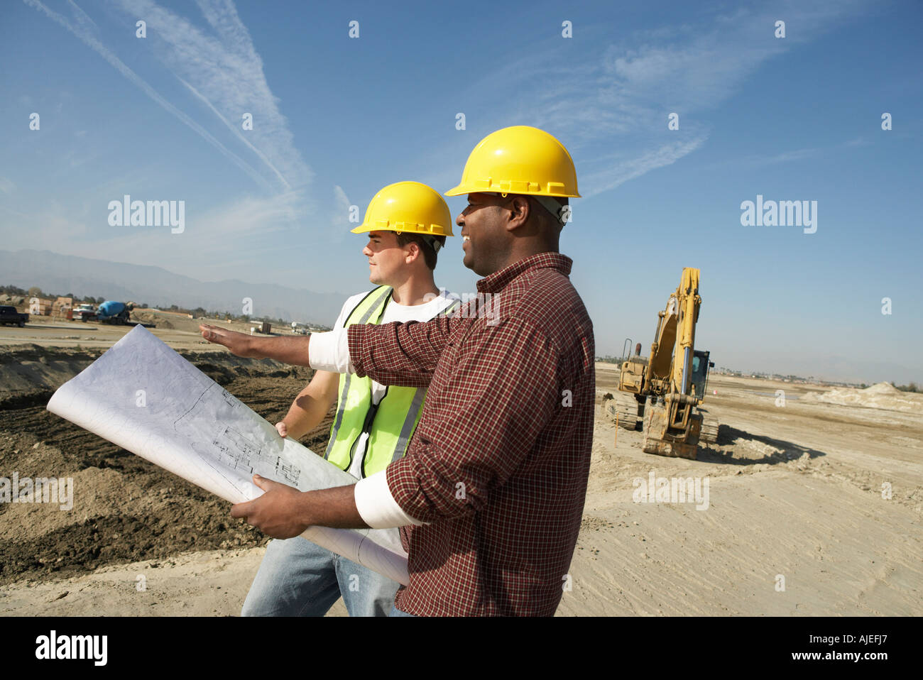 Bauarbeiter tragen Schutzhelme, Blick auf Plan vor Ort Stockfoto