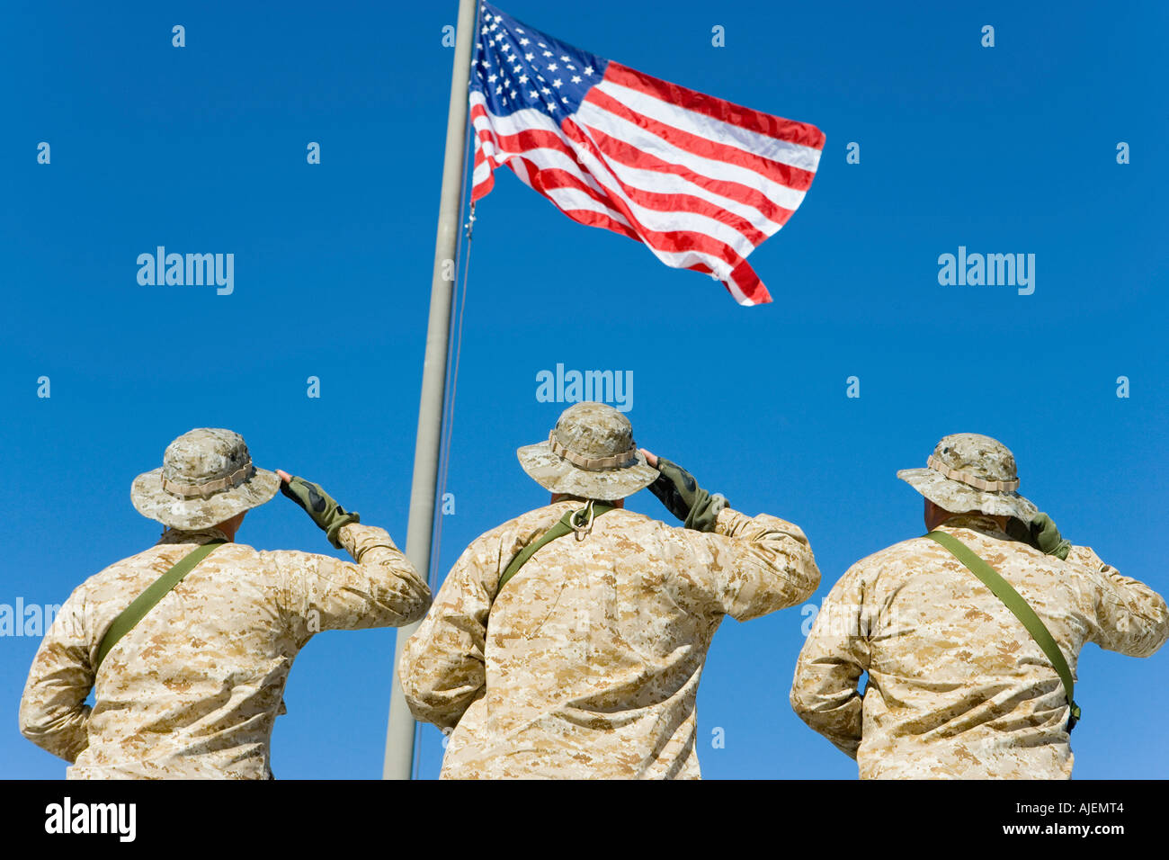 Rückansicht der drei US-Militärpersonal salutieren, die amerikanische Flagge gegen strahlend blauen Himmel Stockfoto