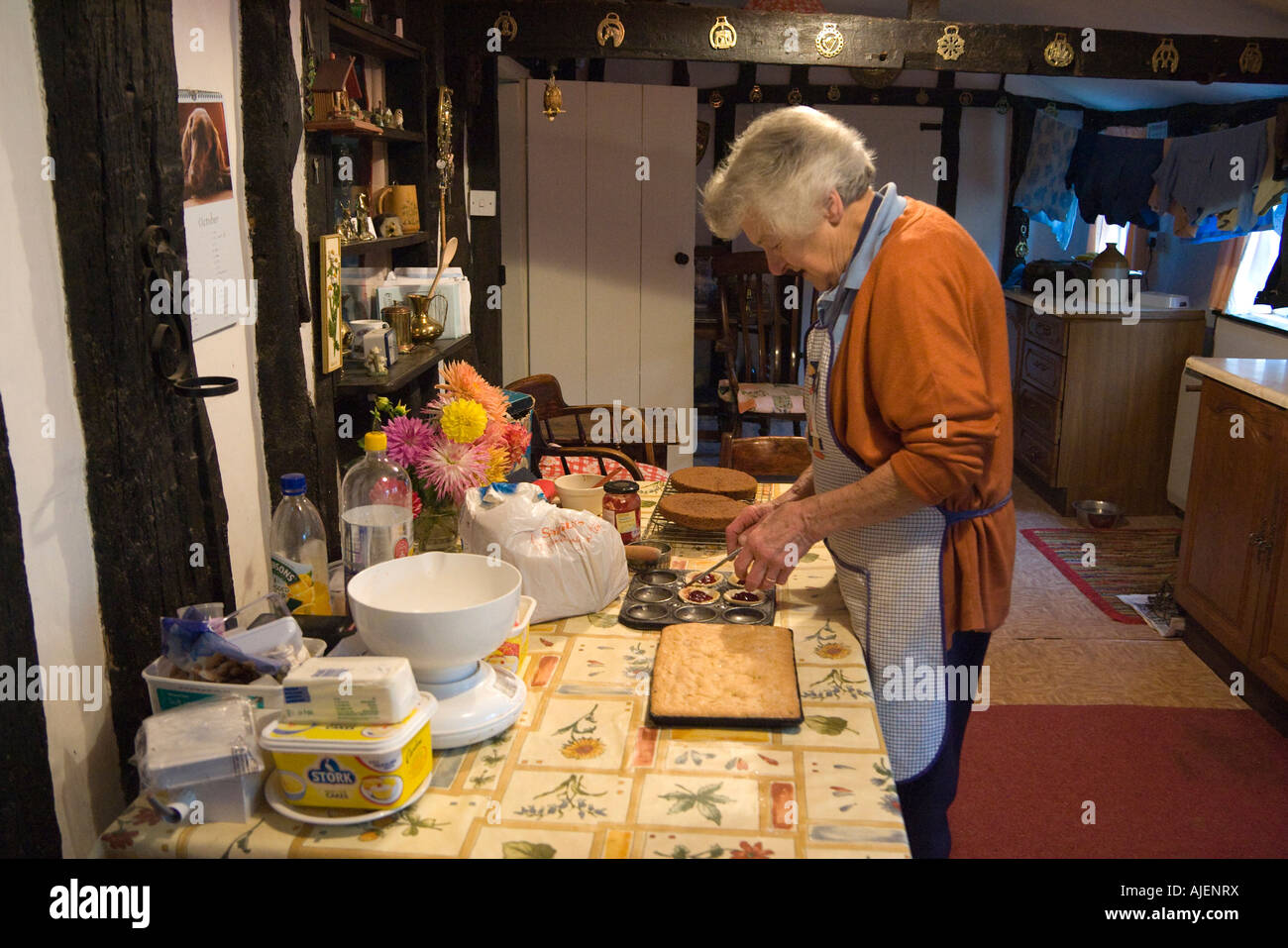 ältere Frau in der Küche des alten tudor-Stil Holz gerahmte Häuschen in einem Dorf von Suffolk, UK Stockfoto