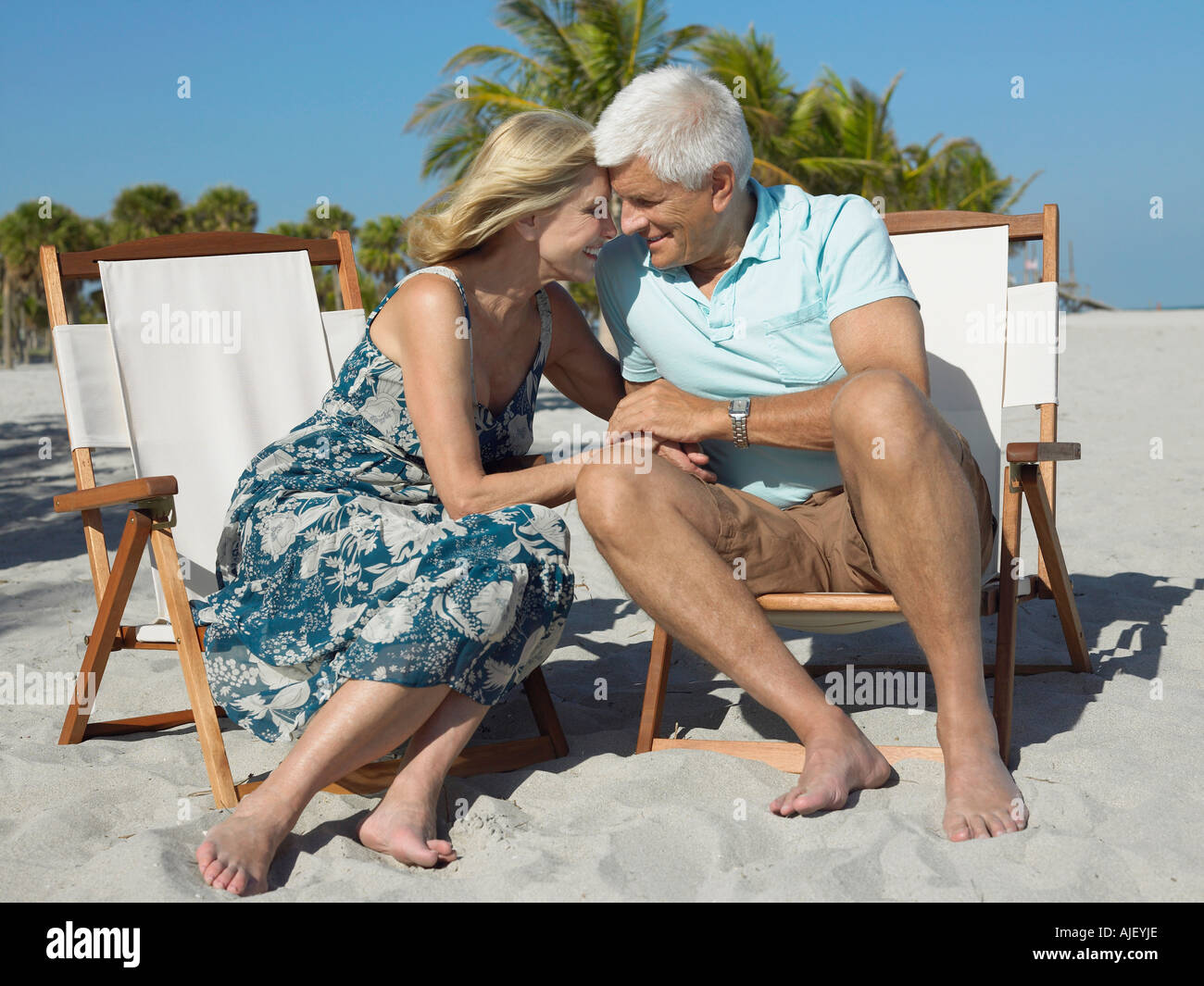 Liebevolle älteres Paar auf Sonnenliegen am Strand, Hand in Hand Stockfoto