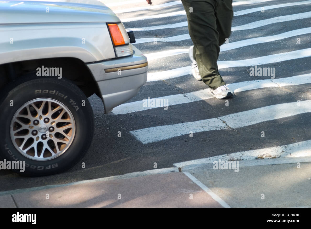 Nahaufnahme der Beine und Füße überqueren einer Straße in den Zebrastreifen vor ein Auto Stockfoto