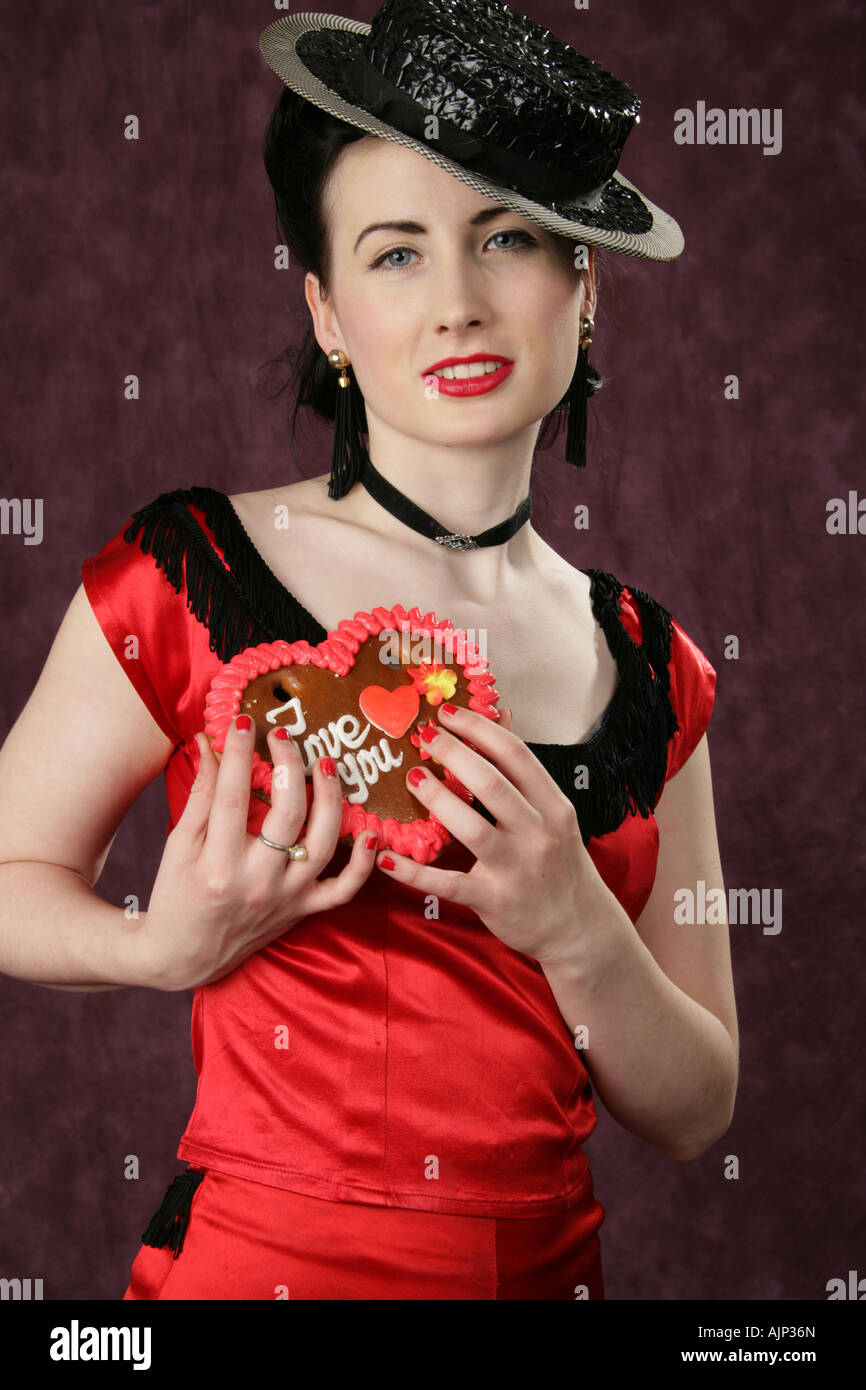 Ein Pin Up Girl in einem schwarzen Hut und roten Kleid hält ein Valentine Herzen Keks Stockfoto