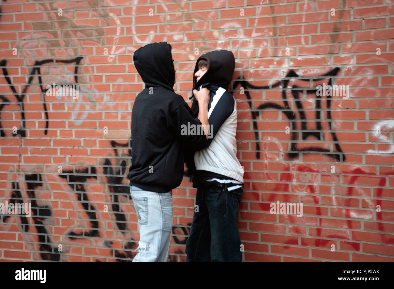 ein Teenager treibt einen jüngeren Jungen gegen eine Wand Stockfoto