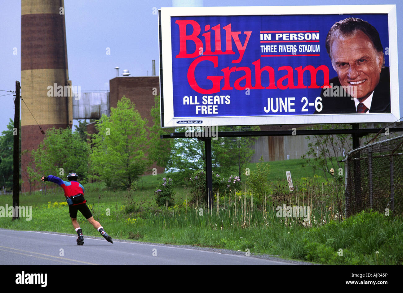 Eine Inline-Skater skatet, vorbei an einer Plakatwerbung einen Auftritt von Evangelist Billy Graham in Pittsburgh, Pennsylvania Stockfoto