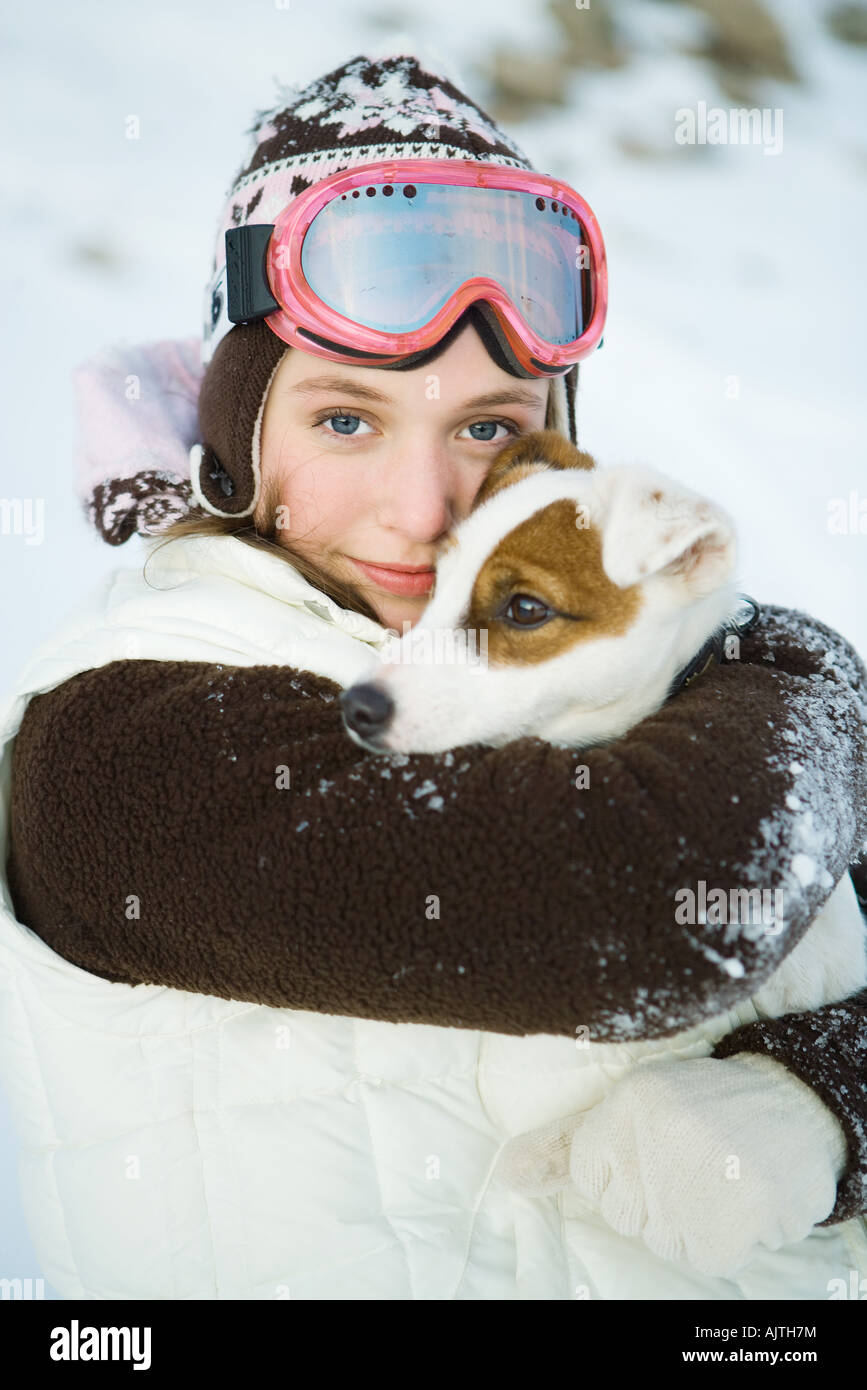 Teenager-Mädchen umarmt Hund, gekleidet in Winterkleidung, lächelnd in die Kamera, Porträt Stockfoto