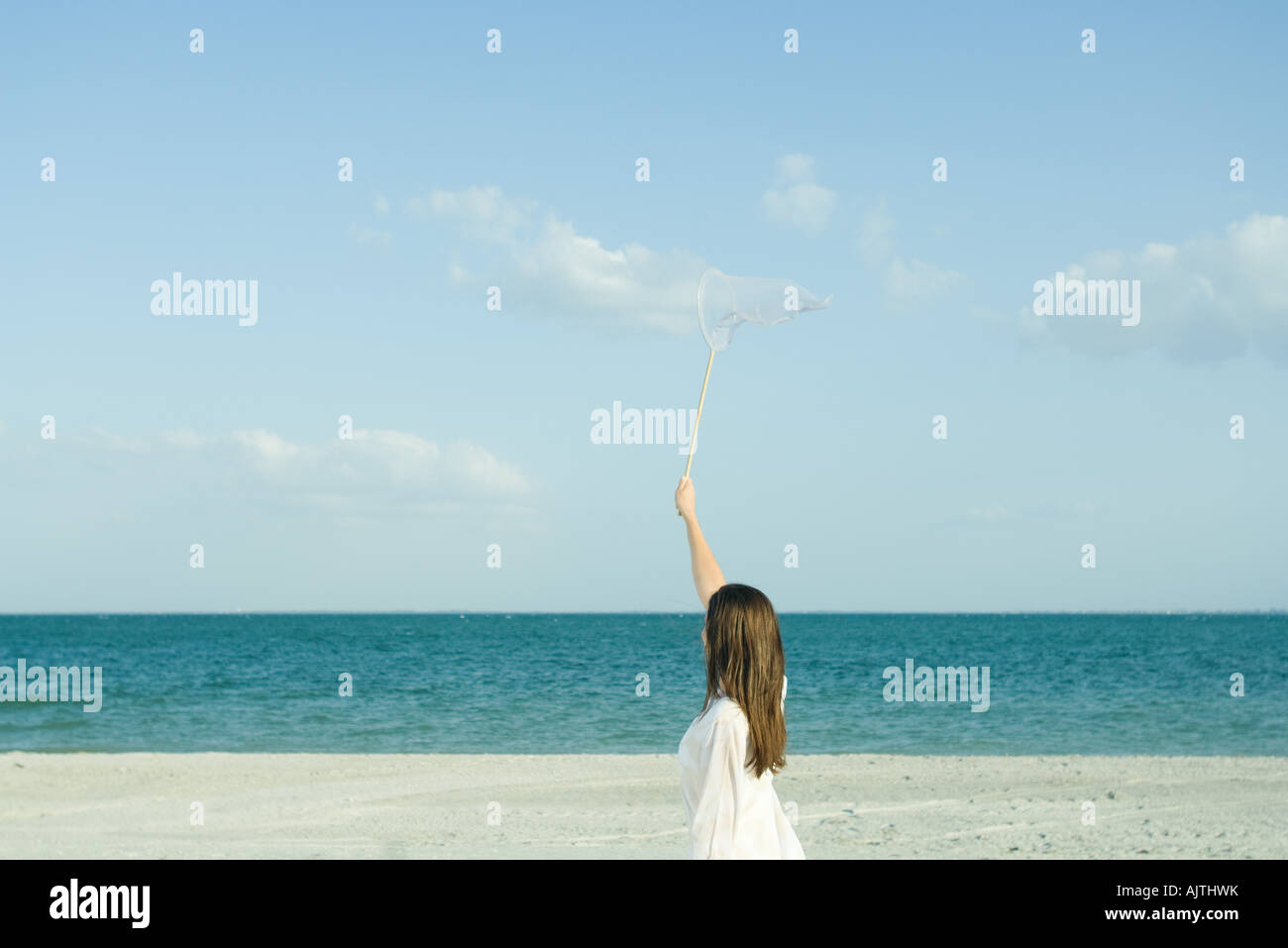 Frau am Strand fangen die Wolken mit Schmetterlingsnetz, Rückansicht, optische Täuschung Stockfoto
