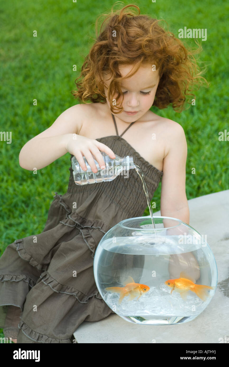 Rothaarige Mädchen gießt Wasser in Flaschen in Goldfischglas Stockfoto