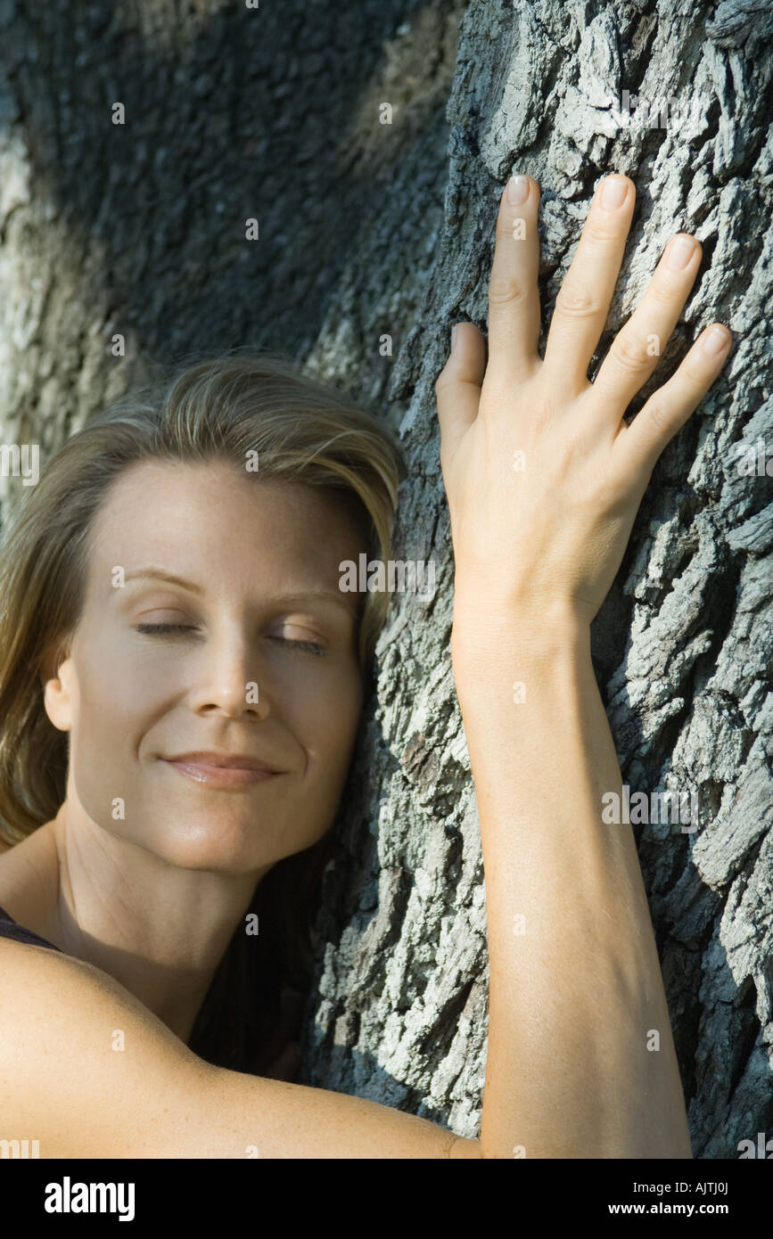 Frau umarmt Baum, Augen geschlossen, lächelnd, Kopf und Schultern Stockfoto