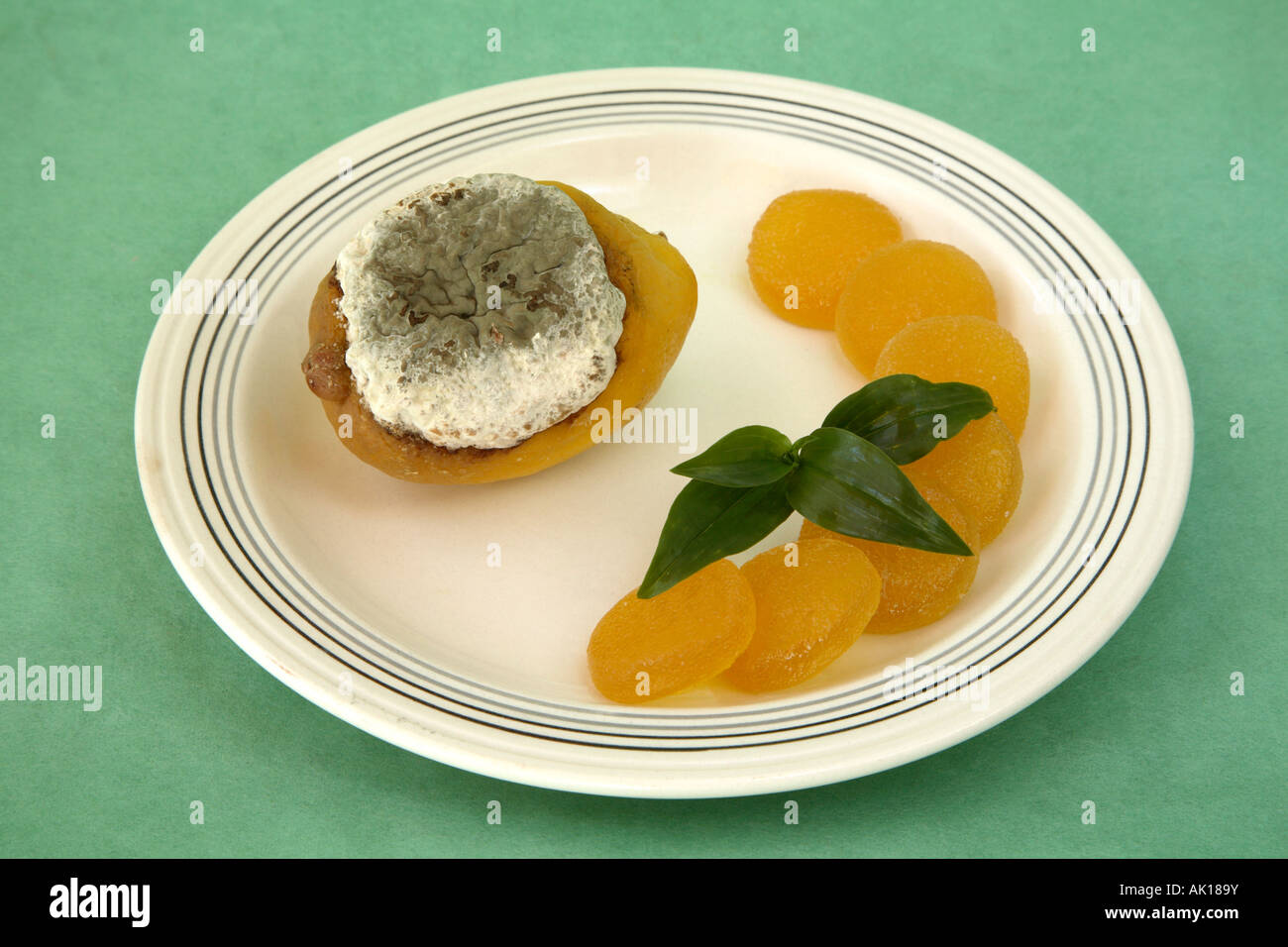 Gelbe Zitrone mit riesigen Schimmel für obere Hälfte der Frucht sowie Halbmond von kreisförmigen Zitrone-Gelee-Bonbons mit Zweig grün. Stockfoto