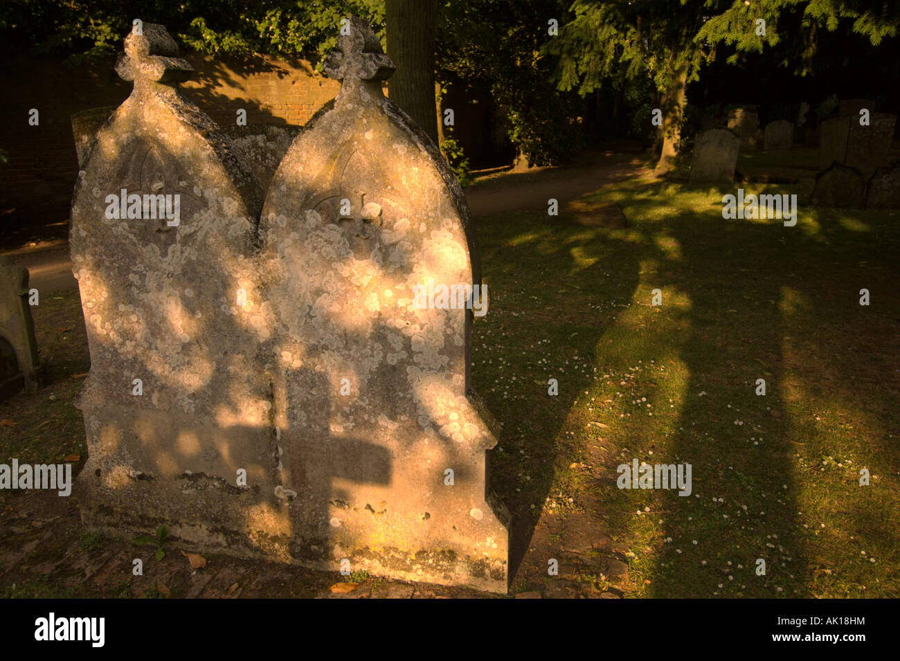 Der Schatten eines Kruzifixes fällt über zwei Grabsteine auf dem Friedhof in England. Stockfoto