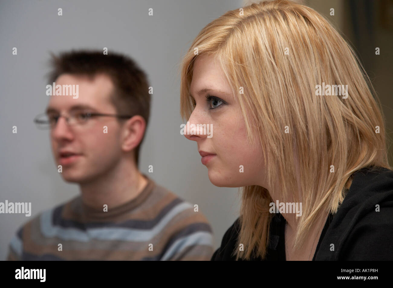 blonde behaarte junge Frau sitzt neben dunkelhaarigen jungen Mann mit Brille jemand anhören Stockfoto