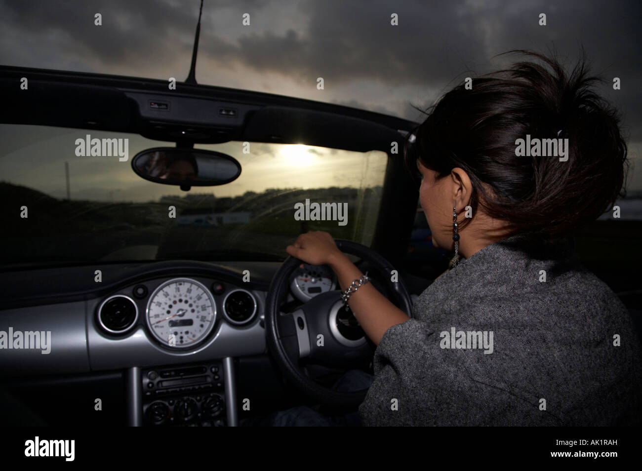 Junge asiatische Frau, die ein Mini Cabrio entlang der Strandpromenade am Abend nach Sonnenuntergang allein das Fahren bei Nacht Stockfoto