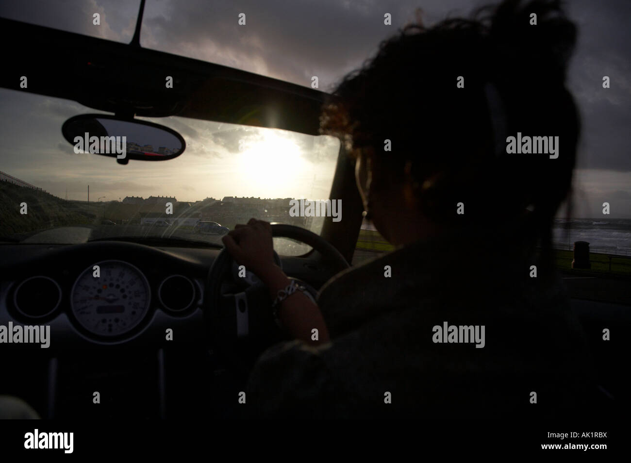 Silhouette der junge Asiatin ein Mini Cabrio entlang der Strandpromenade am Abend in Richtung Sonnenuntergang fahren Stockfoto