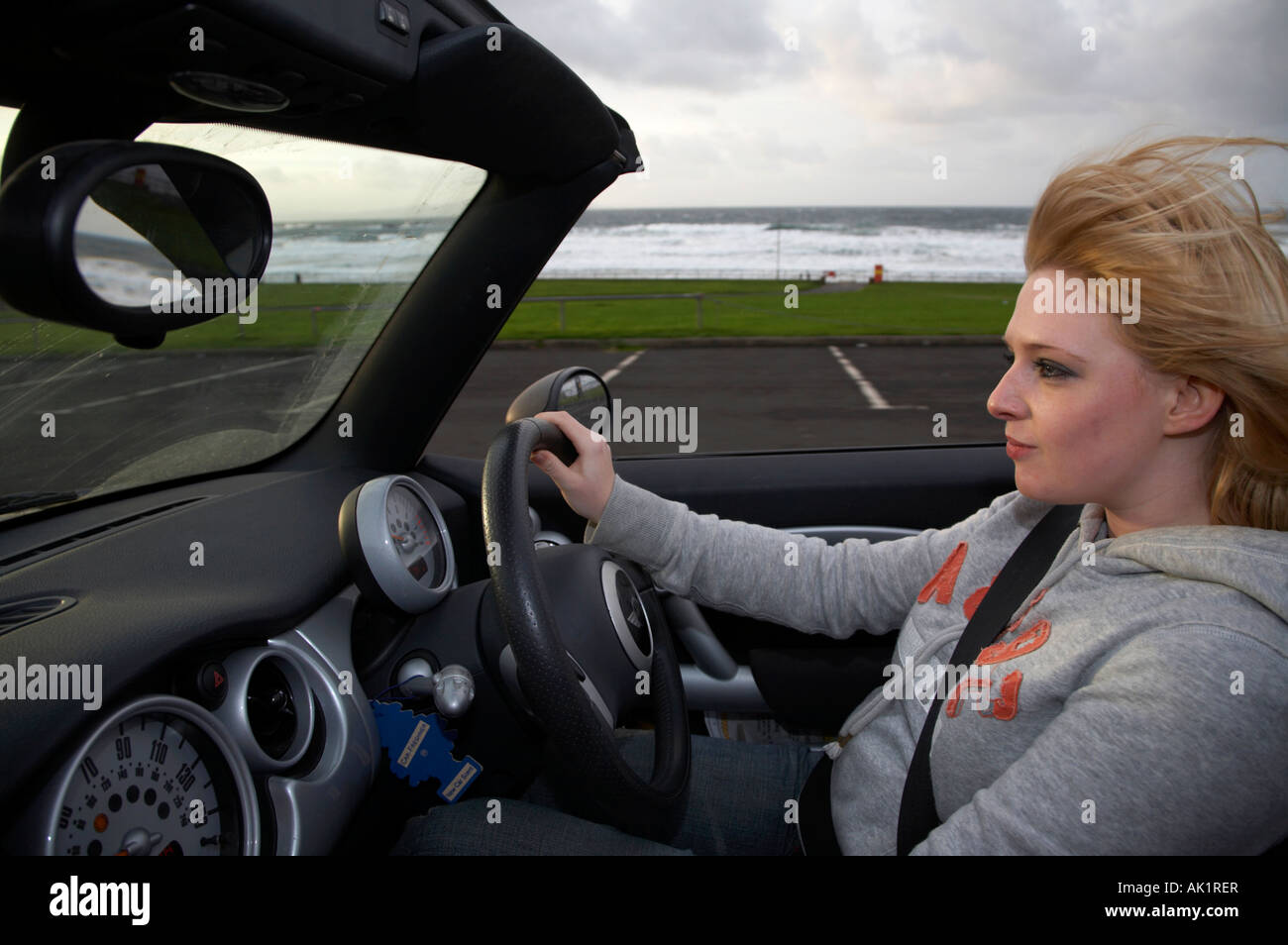 junge blonde behaarte Irin ein Mini Cabrio entlang der Strandpromenade am Abend mit Geschwindigkeit fahren Stockfoto