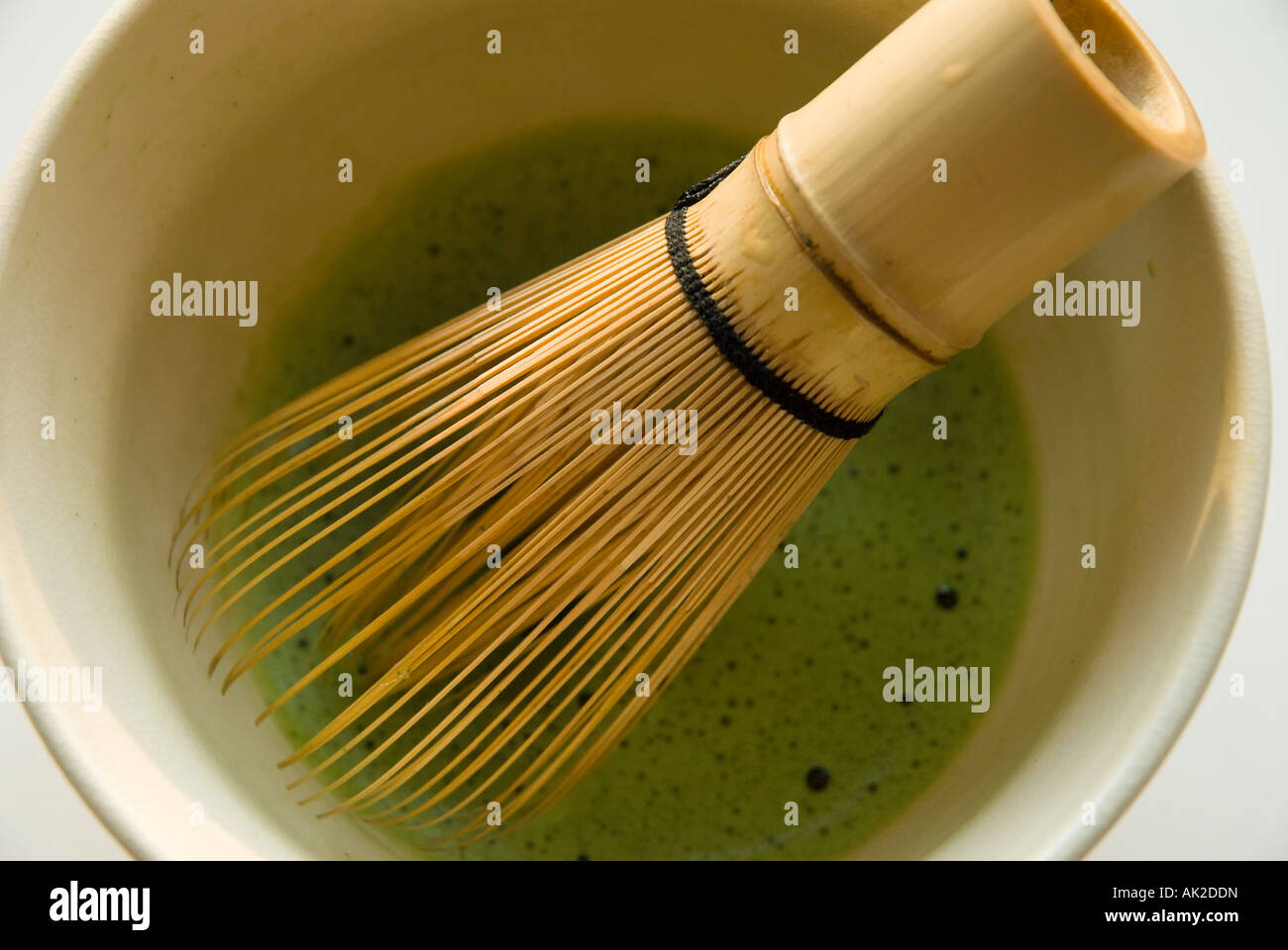 Ein Bambusschläger oder eine Jagd ruht in schaumhaltigem grünem Tee in einer cremefarbenen Teeschale, während Matcha zubereitet wird. Stockfoto