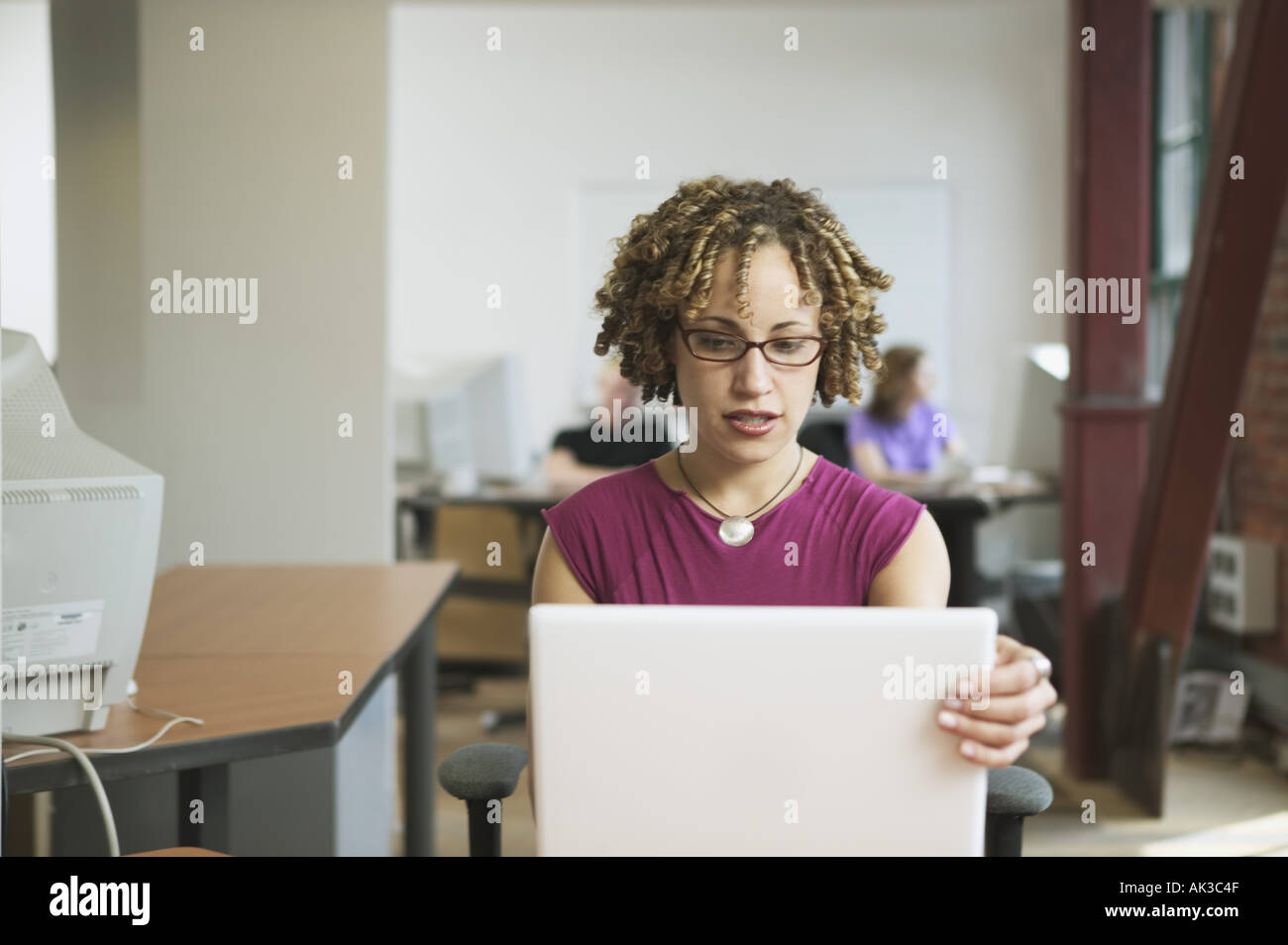 Sitzen an ihrem Schreibtisch, eine Multi-ethnische Frau der 20er Jahre Computer arbeitet Stockfoto