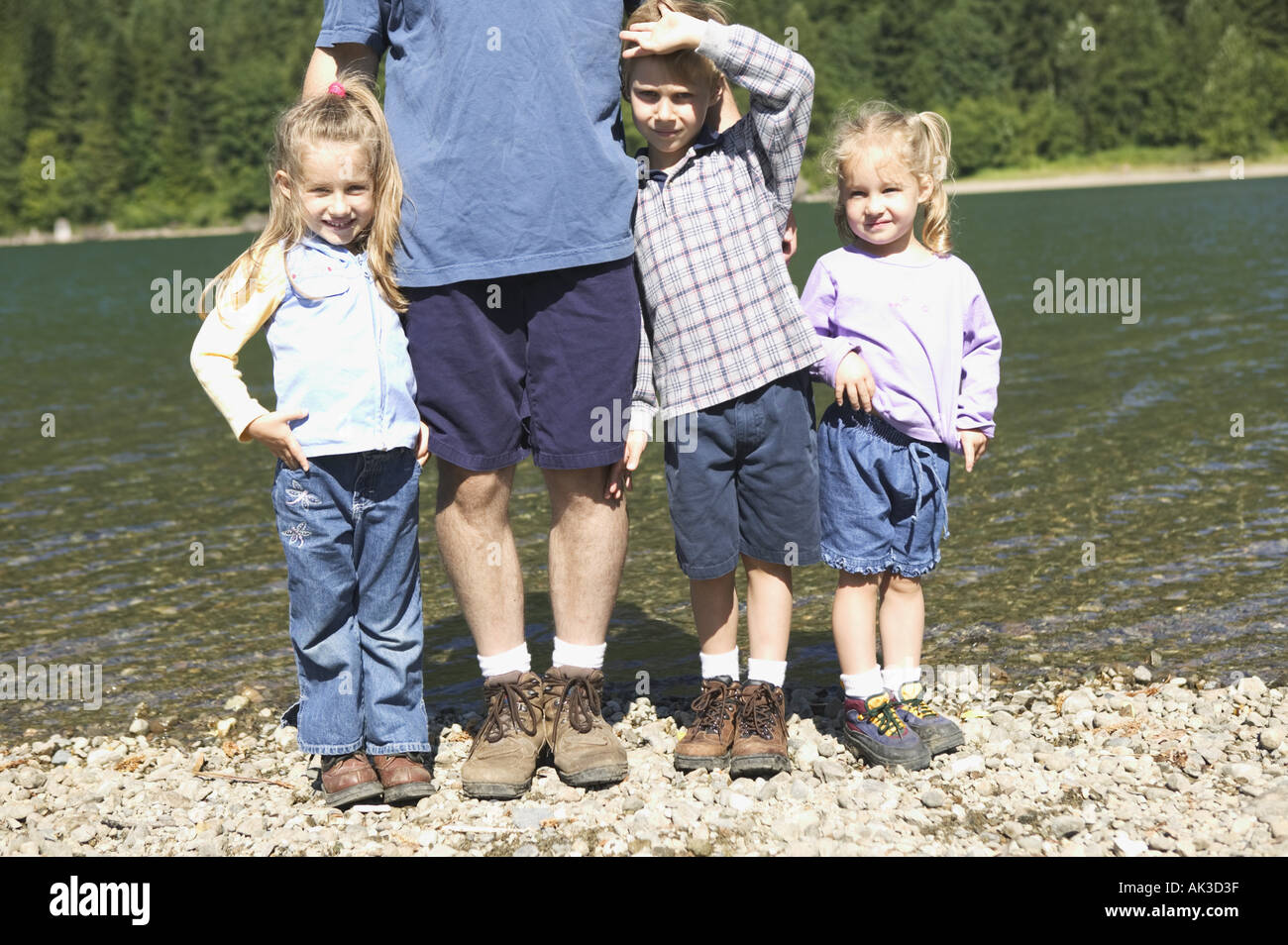 Drei Kinder stehen mit ihrem Vater an einem See Stockfoto