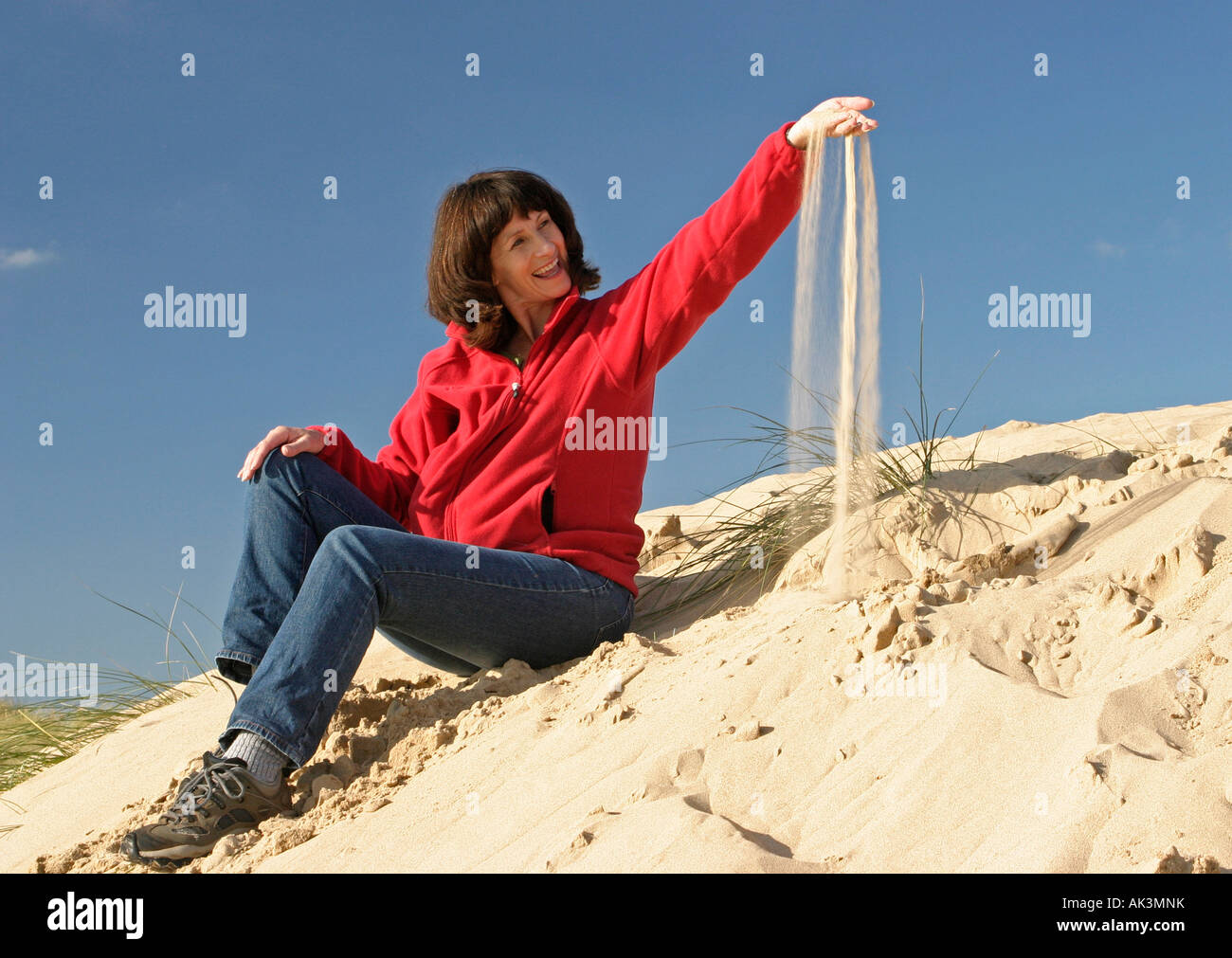 Eine Frau sitzt auf einer Sanddüne Filtern Sand durch ihre Finger lächelnd Stockfoto