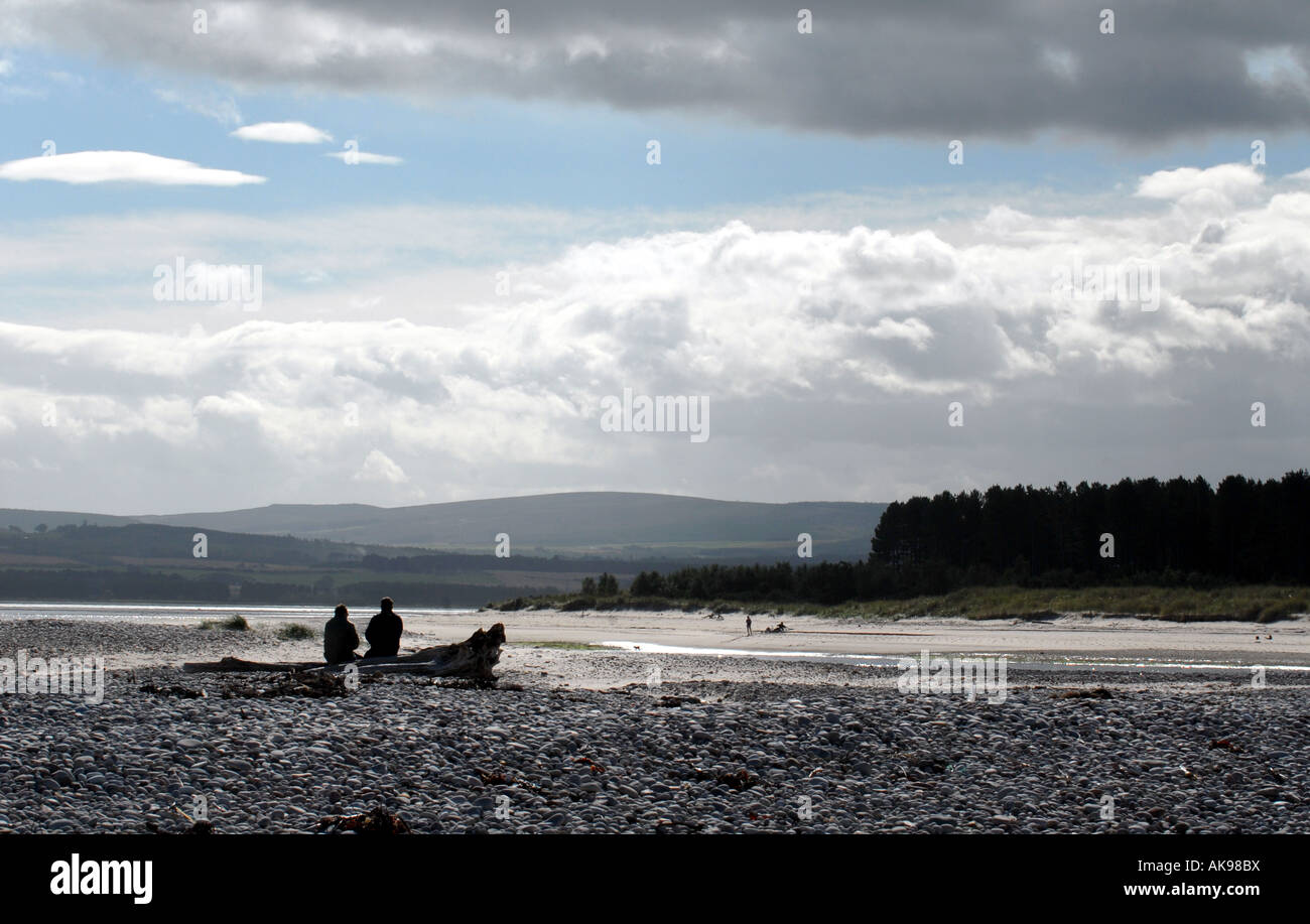 TOURISTEN MACHEN SIE EINE PAUSE AUF EINEM BAUMSTAMM IN FINDHORN BAY AUF DER NORDÖSTLICHEN SCHOTTISCHEN KÜSTE IN DER NÄHE VON INVERNESS.UK Stockfoto
