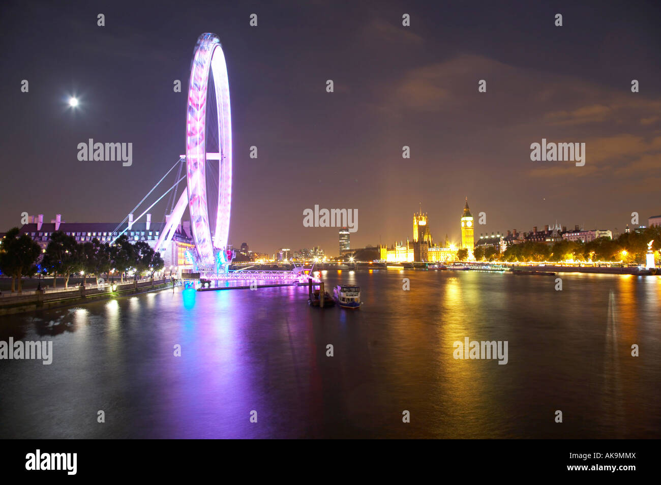 Blick auf das London Eye und die Houses of Parliament entlang der Themse von Hungerford Bridge bei Nacht, London Stockfoto