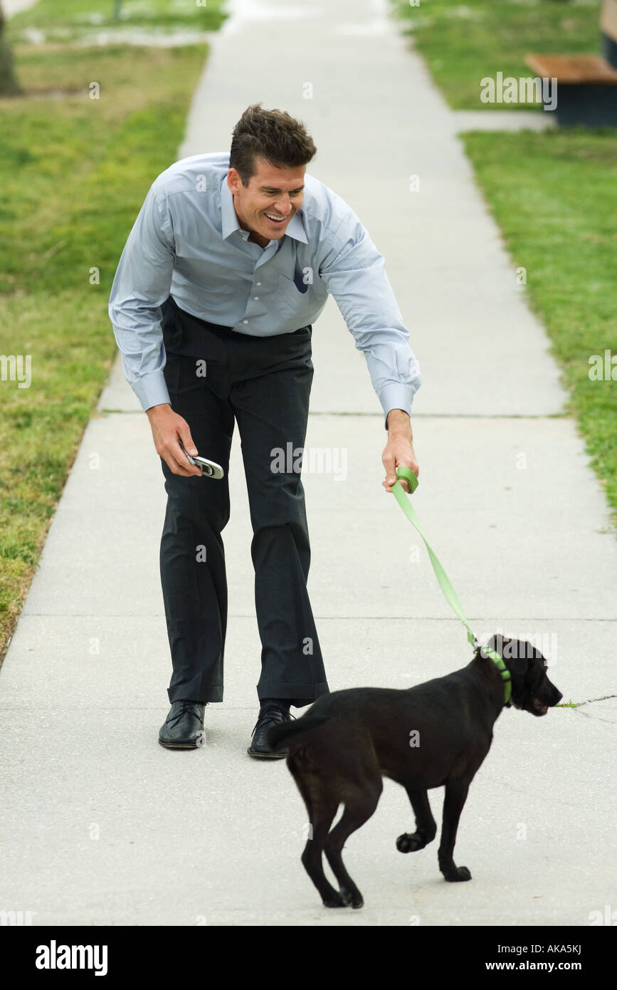 Mann zu Fuß Hund auf Bürgersteig, nach vorne beugen, Lächeln Stockfoto