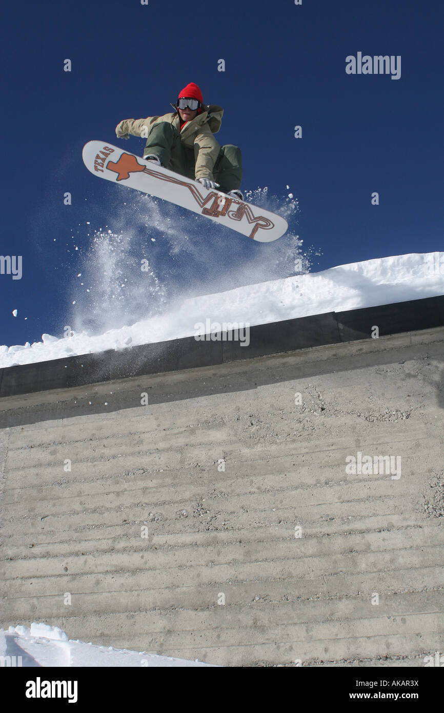 Snowboarder springt eines kleinen Gebäudes zu Boden unten, tiefblauer Himmel und Schnee-Spray. Stockfoto