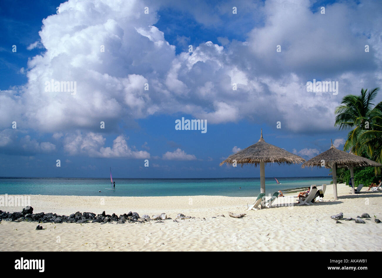 Strohgedeckte Sonnenschirme am Strand mit Windsurfer im Meer Malediven Indischer Ozean Stockfoto