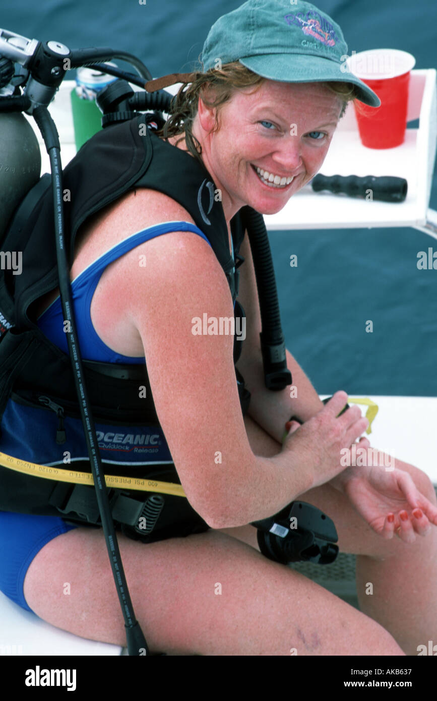 Eine kaukasische rote Kopf Frau lacht und lächelt, als sie auf ein weißes Boot Sitz tragen einen grünen Baseball Kappe Tauchausrüstung sitzt ein Stockfoto