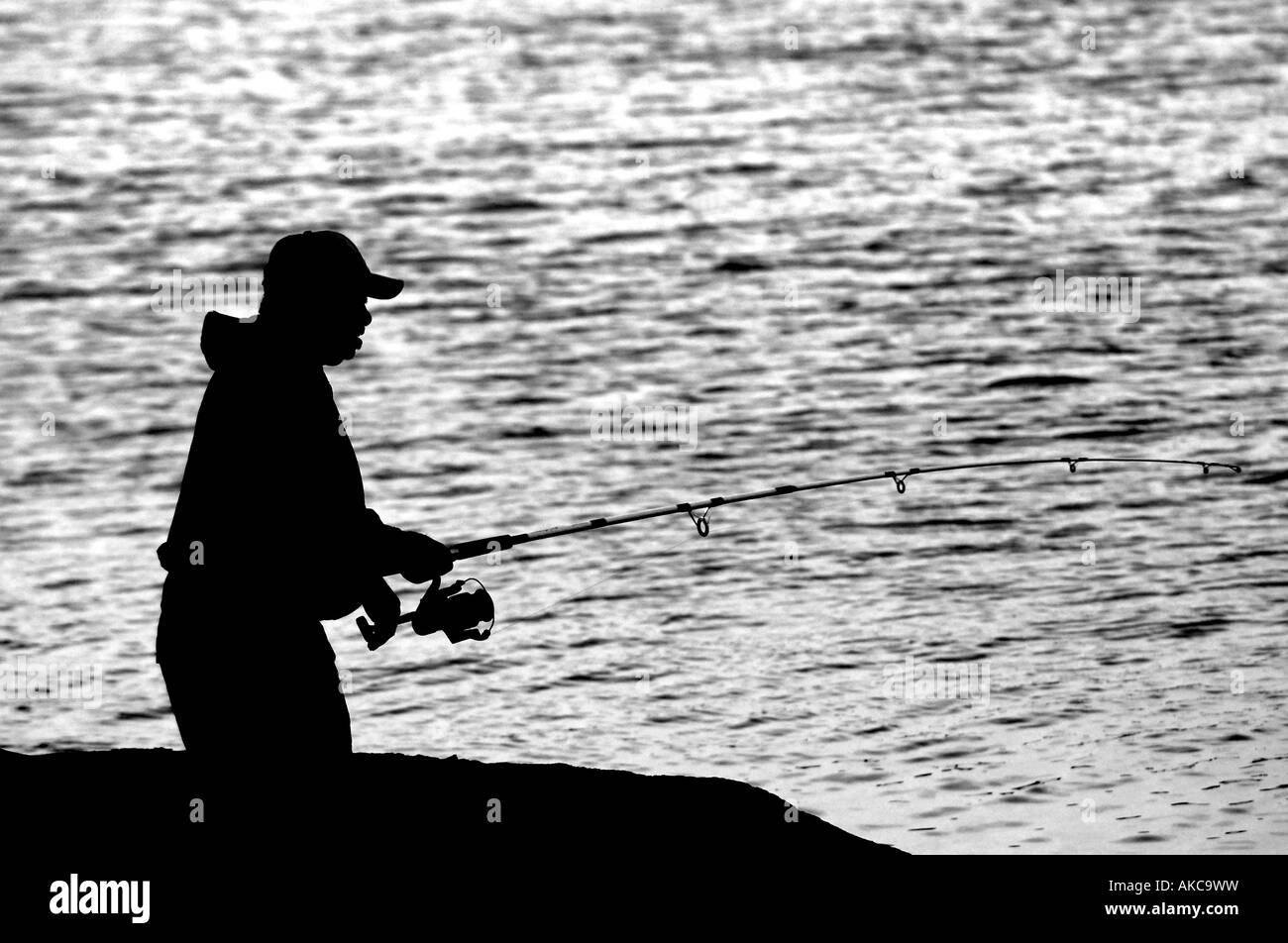 Ein Mann Fische vom Ufer Silhouette durch Wasser Stockfoto