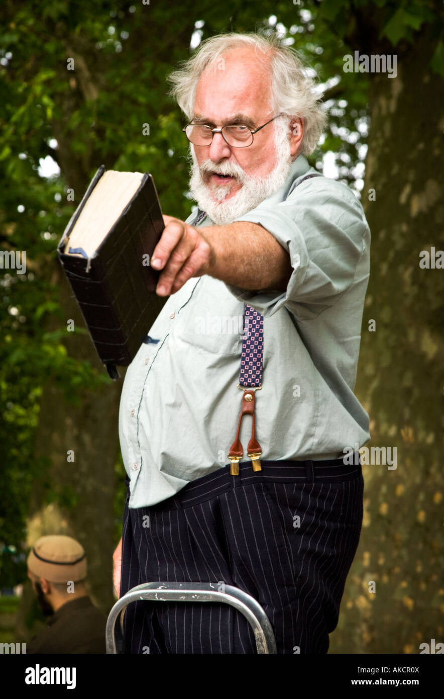 Einen weißen Bart christlicher Prediger an Sprechers Ecke mit einer Bibel in der hand. Ein muslimischer Mann ist hinter gesehen. Stockfoto