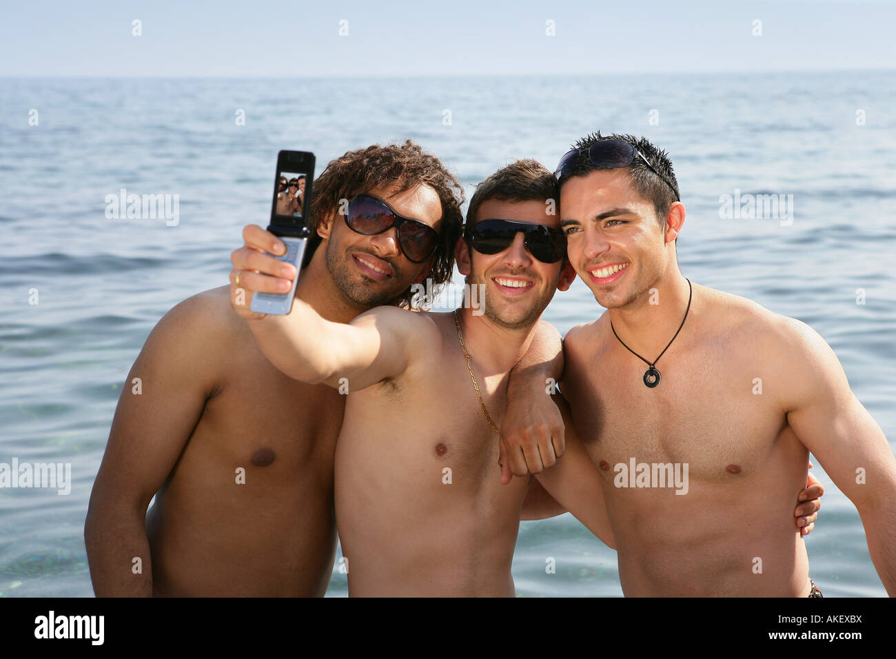 junge Männer am Strand mit Handy Stockfoto