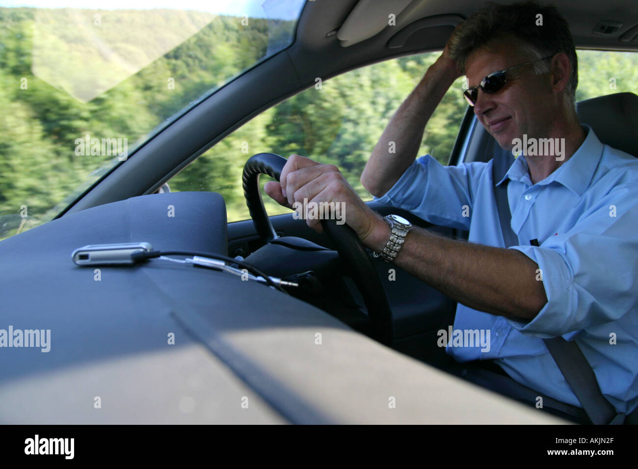 Innenaufnahme des mittleren gealterten männlichen fahrendes Auto suchen verärgert mit MP3-Player auf Armaturenbrett Stockfoto