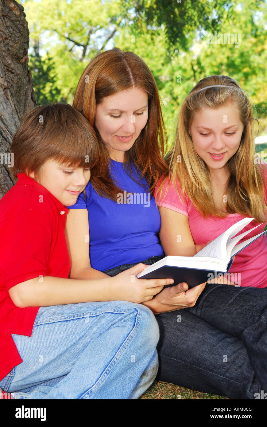 Familie Mutter und Kinder lesen ein Buch unter einem Baum im Sommerpark Stockfoto