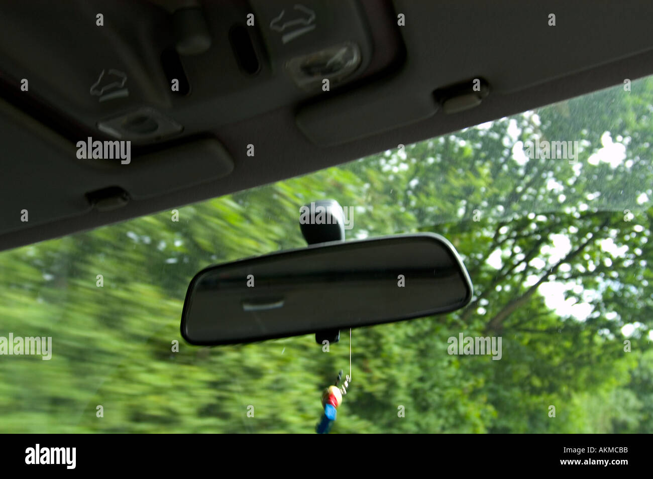 Blick auf ein Auto s überprüfen Spiegel mit Ornament hängen und verschwommen Bäume im Hintergrund zeigt die Geschwindigkeit des Autos Stockfoto