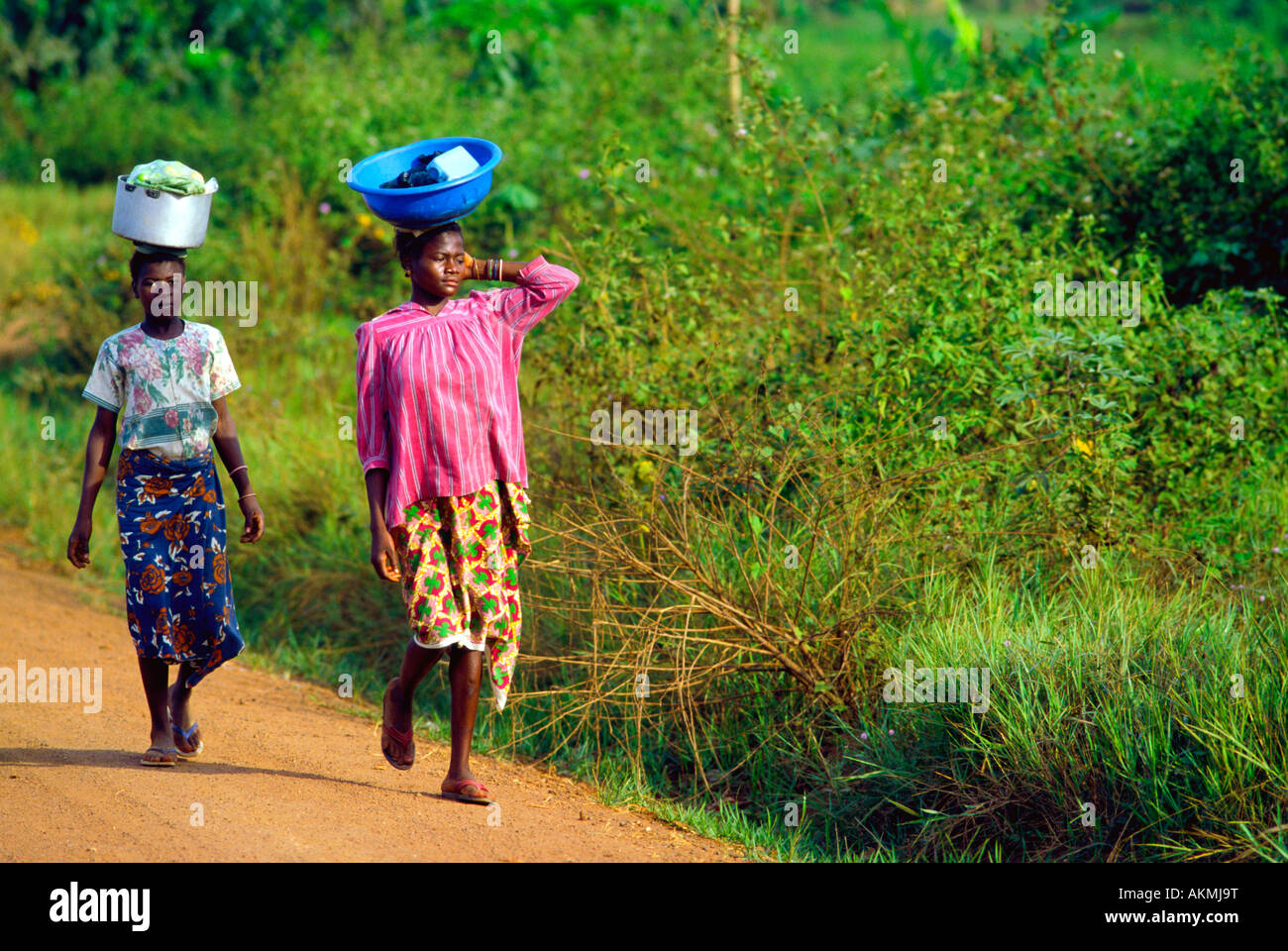 Zwei Frauen balancieren ihr Hab und gut auf den Kopf bei einem Spaziergang entlang einer unbefestigten Straße in die Stadt Stockfoto