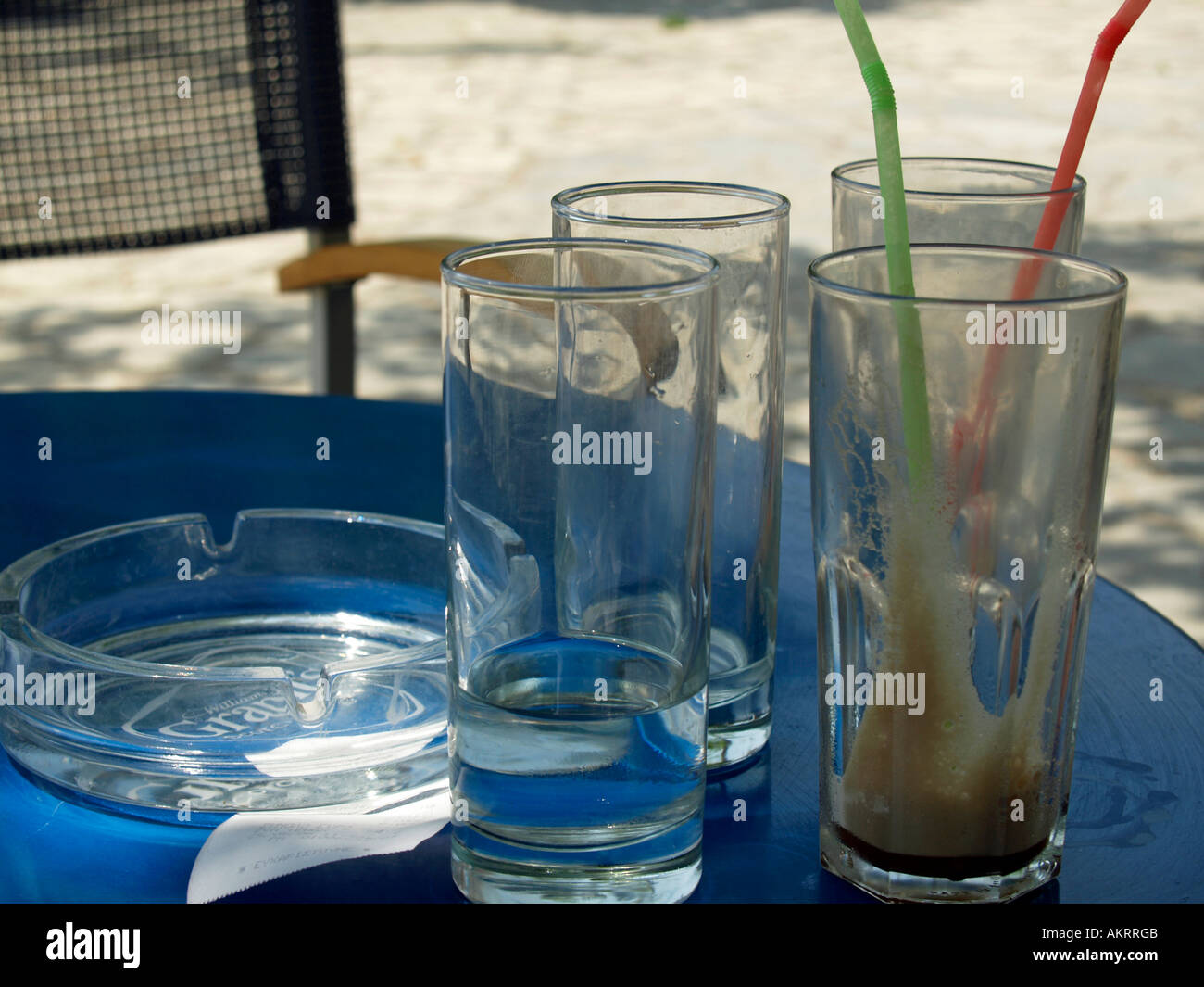zwei leere Gläser Frappe Frappé kalter Kaffee mit Schaum und zwei leere Gläser Wasser mit Bill und Aschenbecher auf dem Tisch Stockfoto