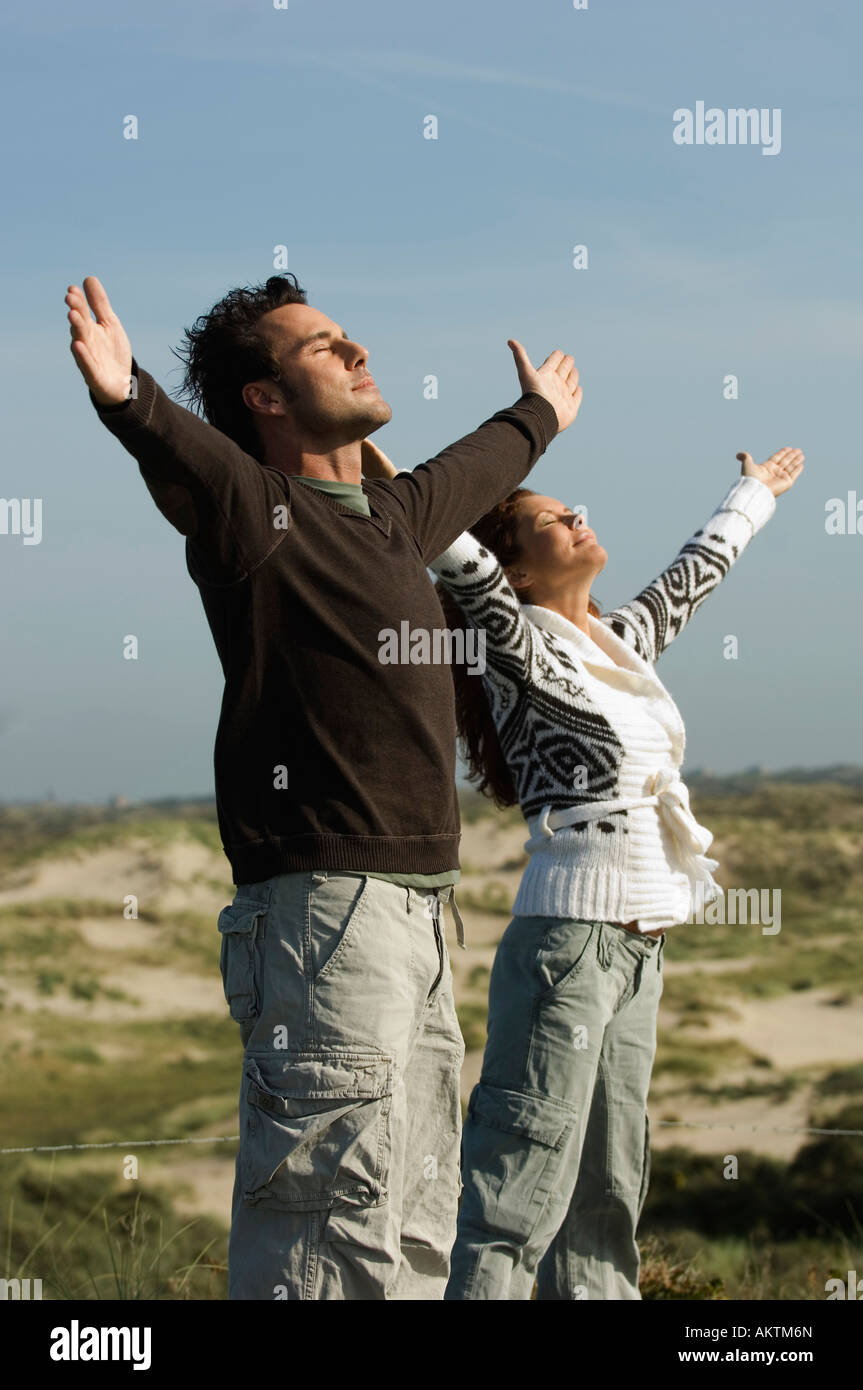 Paar stehend mit Armen verteilt in Dünen, Seitenansicht Stockfoto