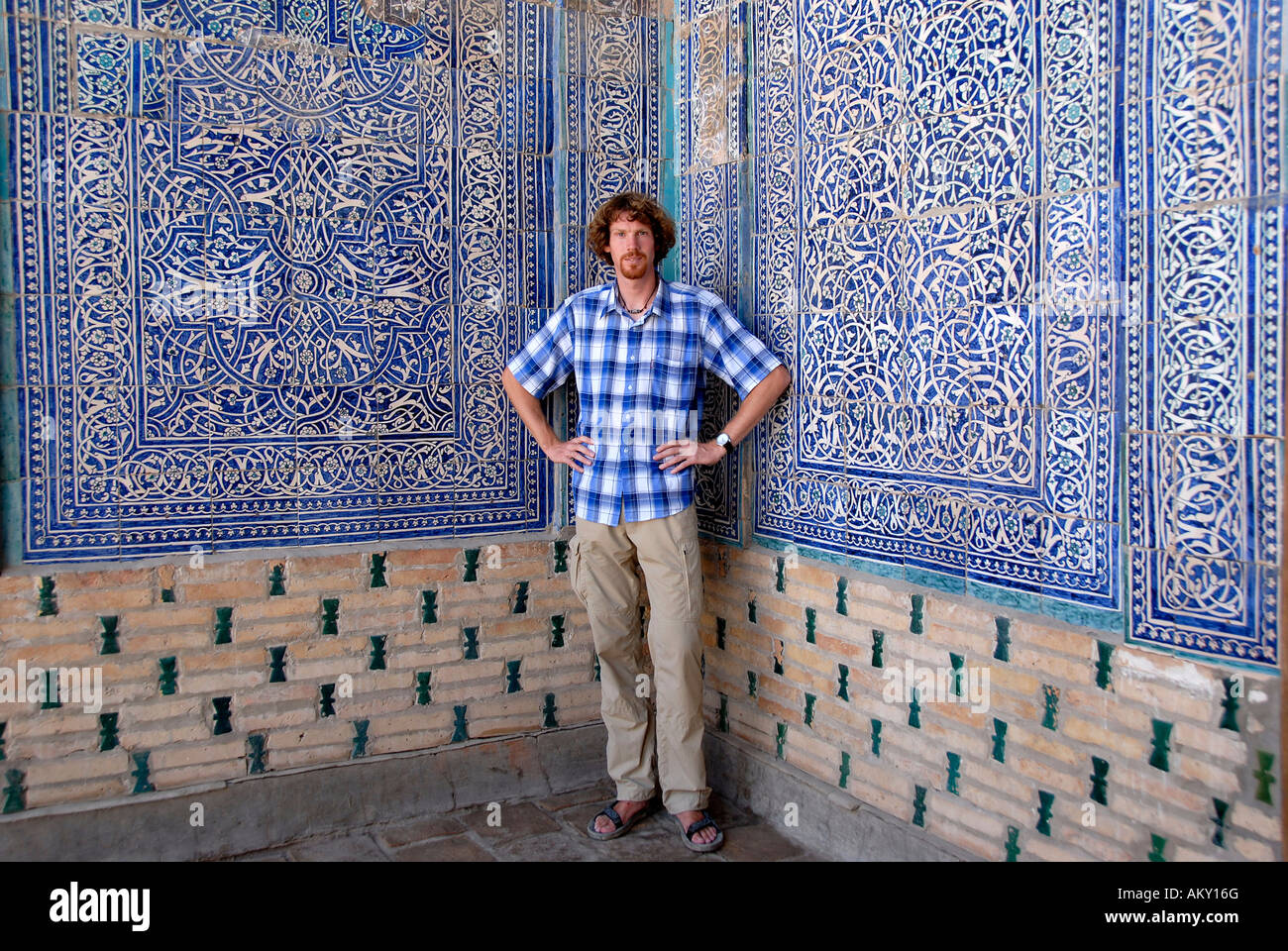 Junger Mann an fein dekorierte Wand mit blauen und weißen Kacheln und Zoroastrian Symbole der Leichtigkeit Tash Hauli Palast Khiva Uzbekistan Stockfoto