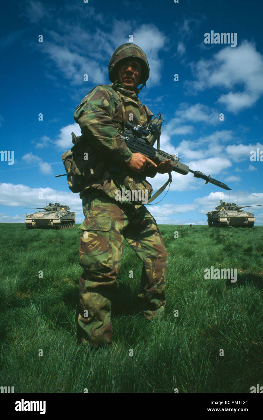 MILITÄRISCHE Ausbildung britische Armee Soldat Tarnung Ruf in einem Feld mit einer Pistole mit zwei Krieger Tanks hinter. Stockfoto