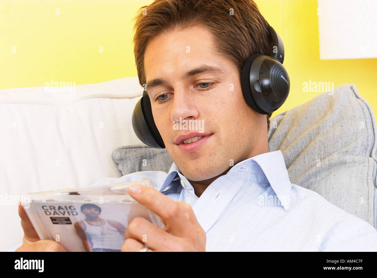 Entspannen Sie sich auf Sofa trägt Kopfhörer und CD-Rom hält Mann Stockfoto